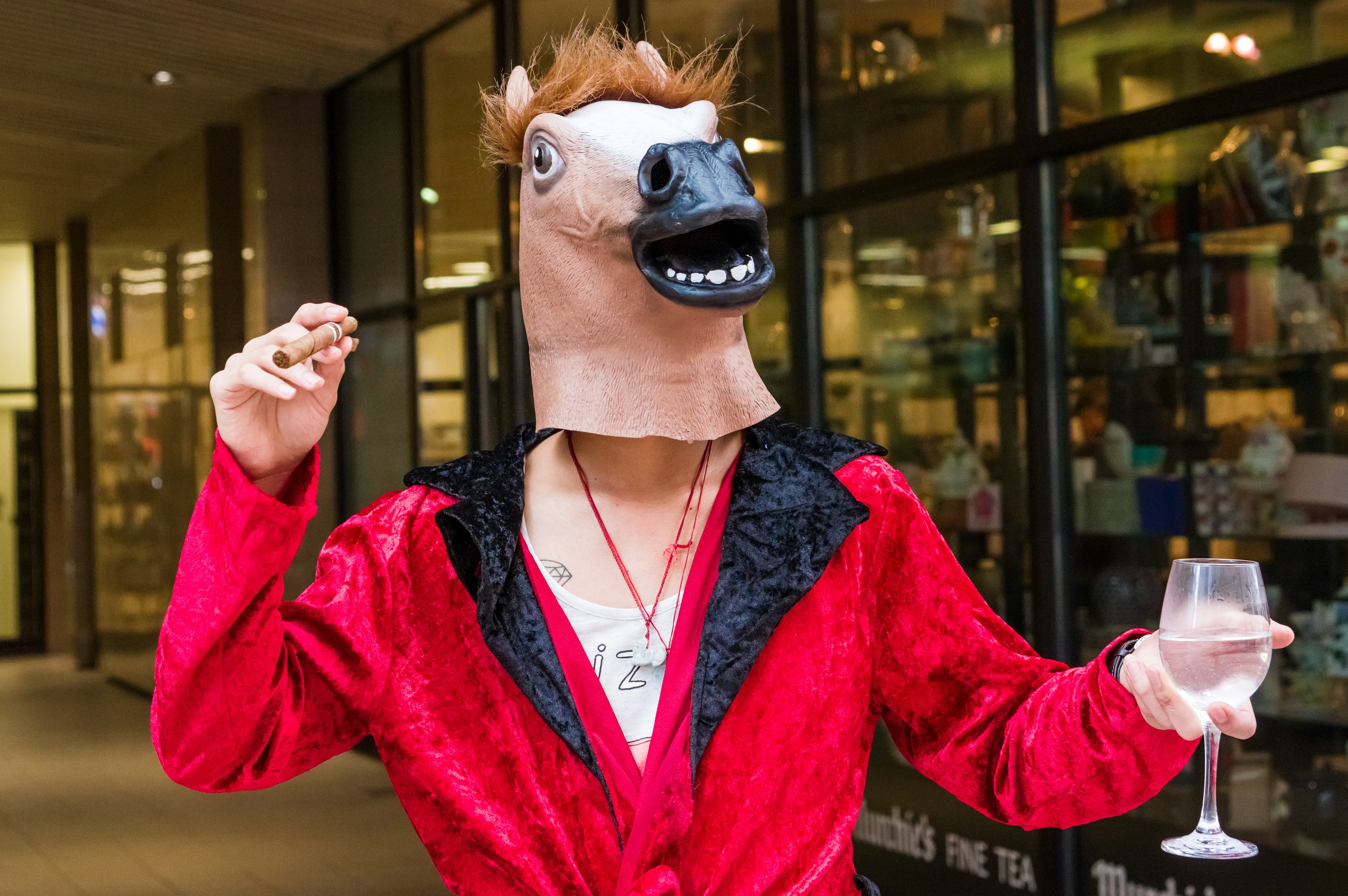 Person wearing a horse mask in a red jacket holding a glass