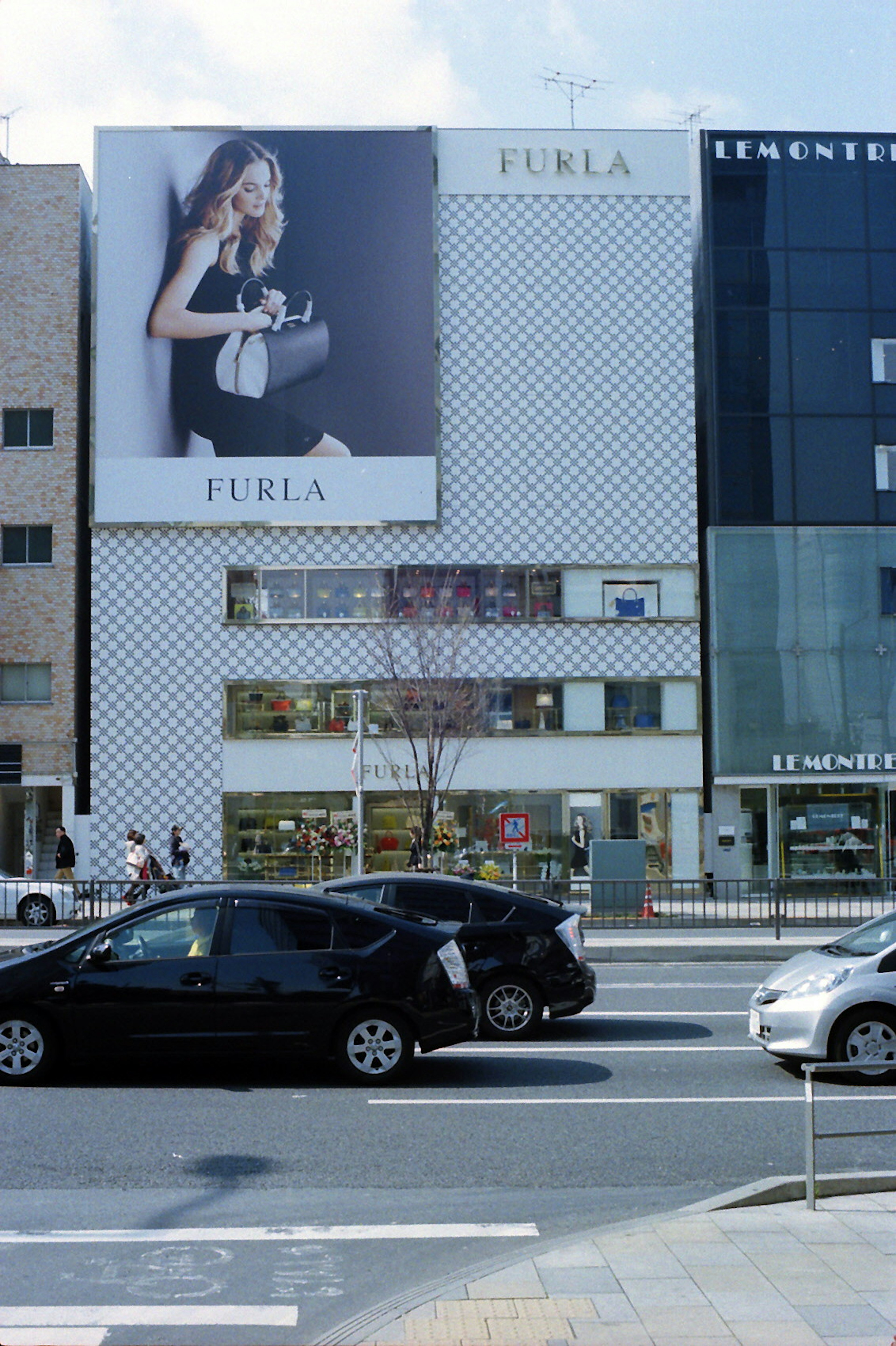 Außenansicht eines Gebäudes mit FURLA-Werbung und Autos auf der Straße