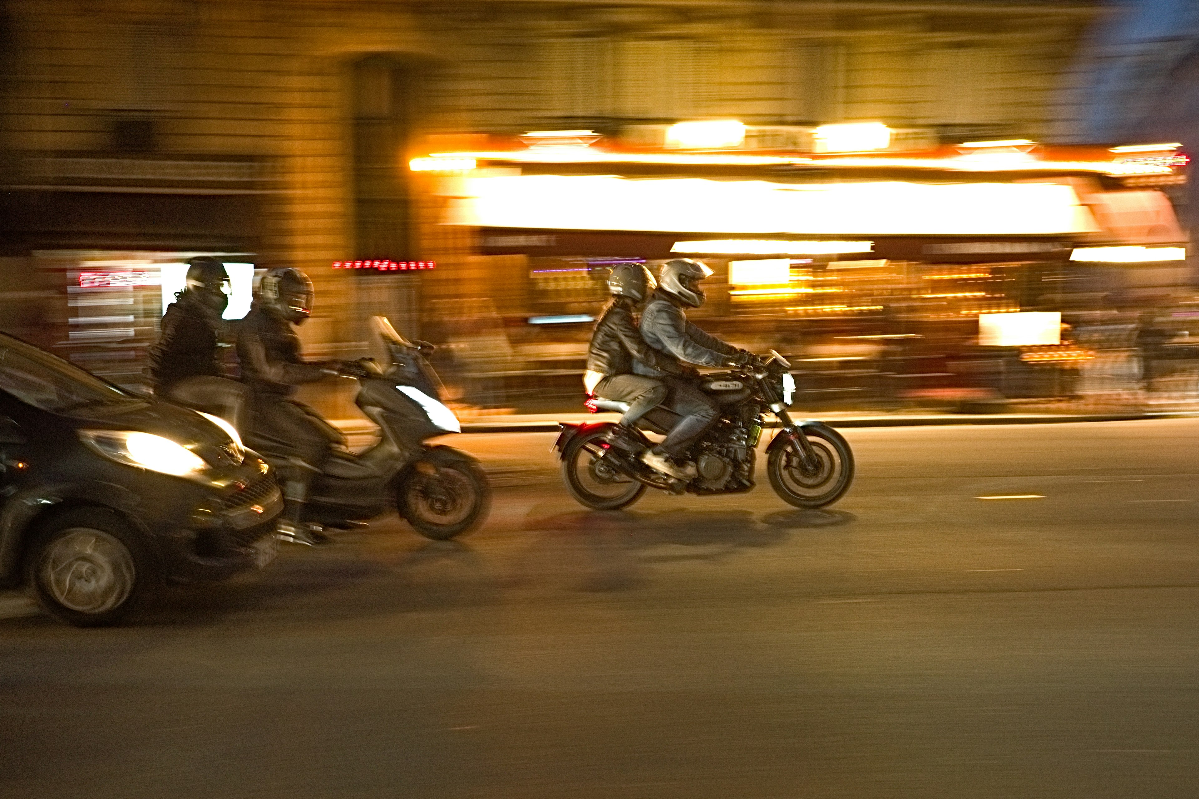 Motorräder, die nachts durch eine Stadt mit warmen Lichtern im Hintergrund fahren