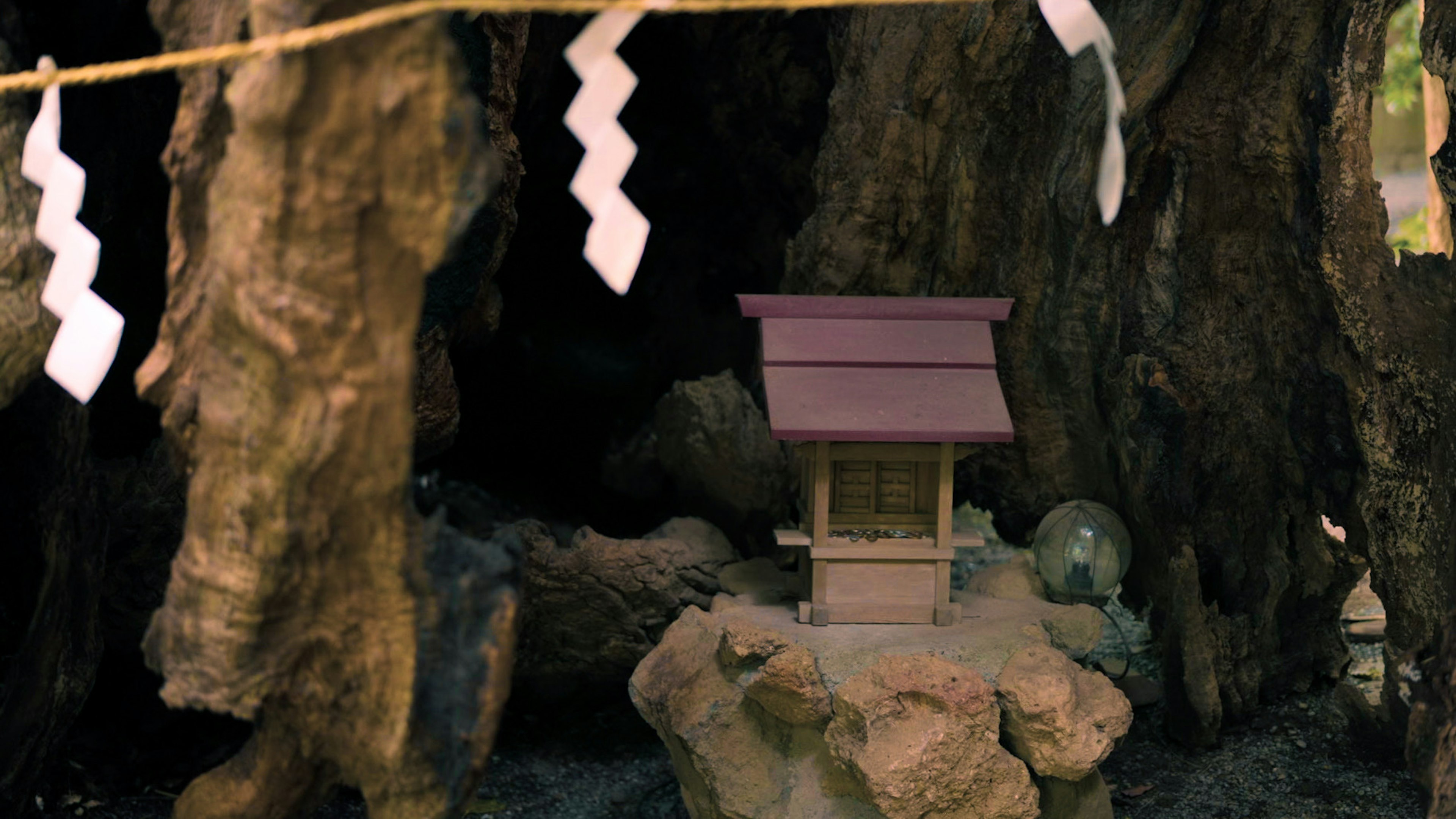 小型神社模型嵌在树木之间， resting on a rock