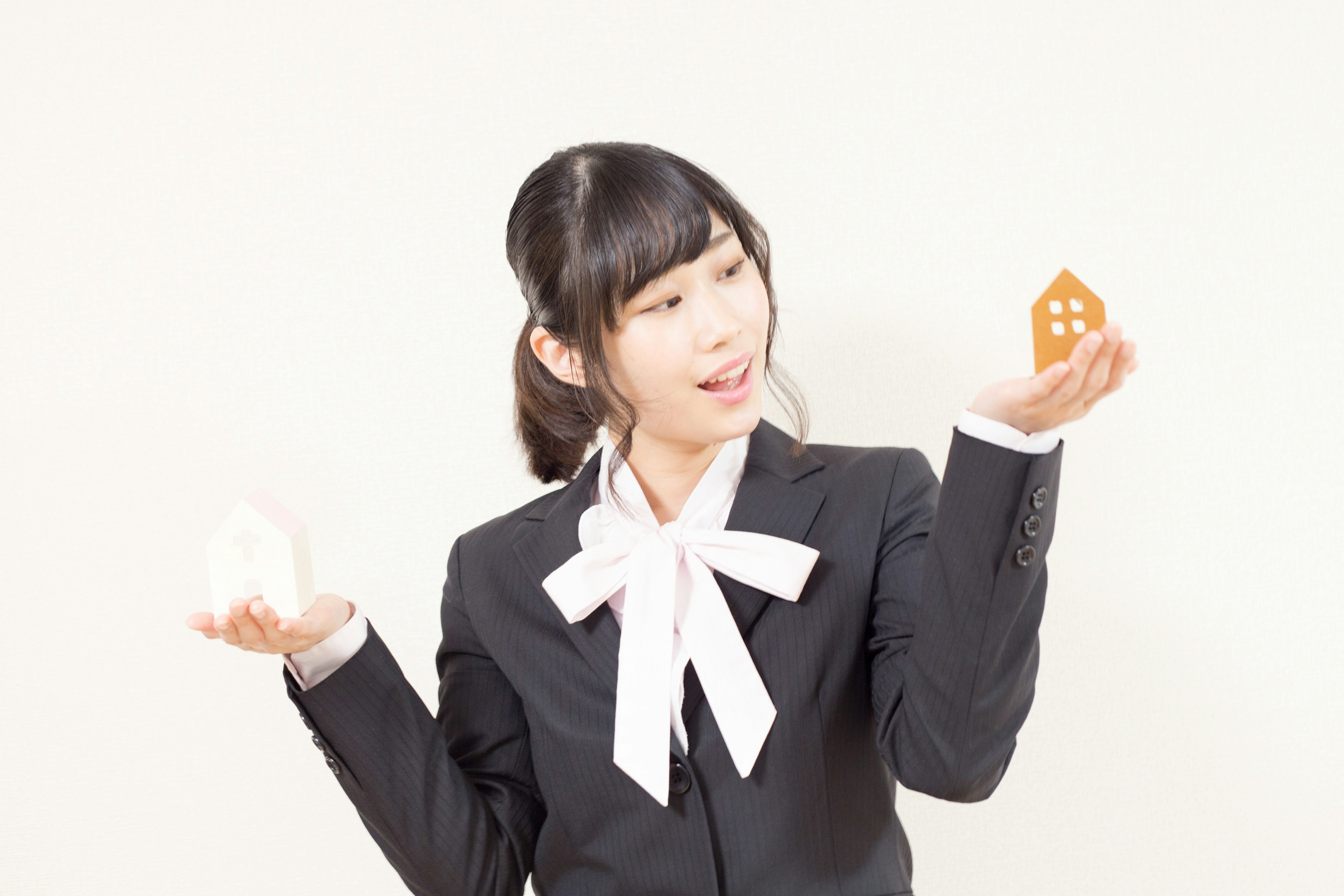 Girl in a suit holding a white house shape and an orange house shape against a white background