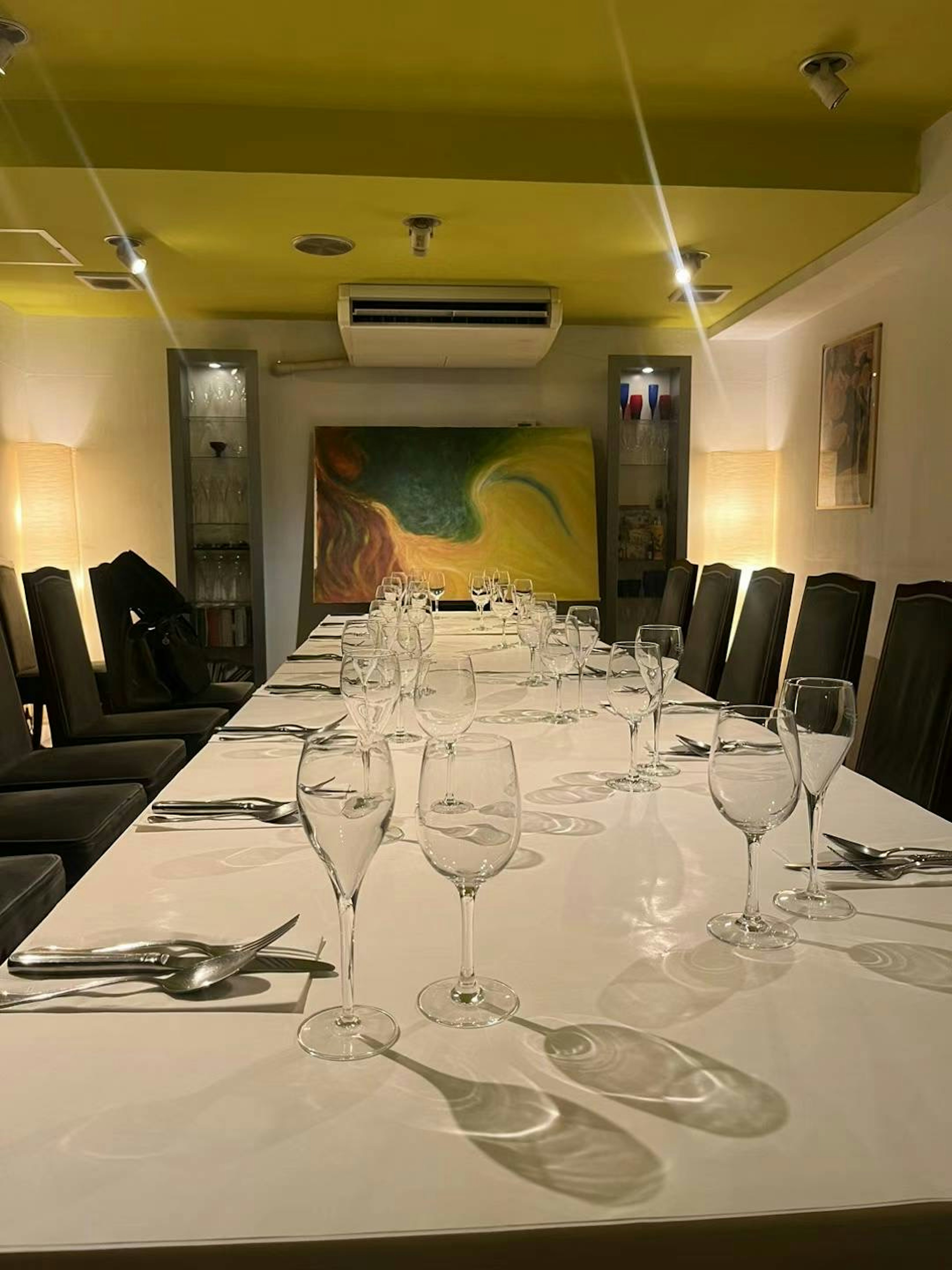 Dining room with a long table set with glasses and cutlery under a bright yellow ceiling