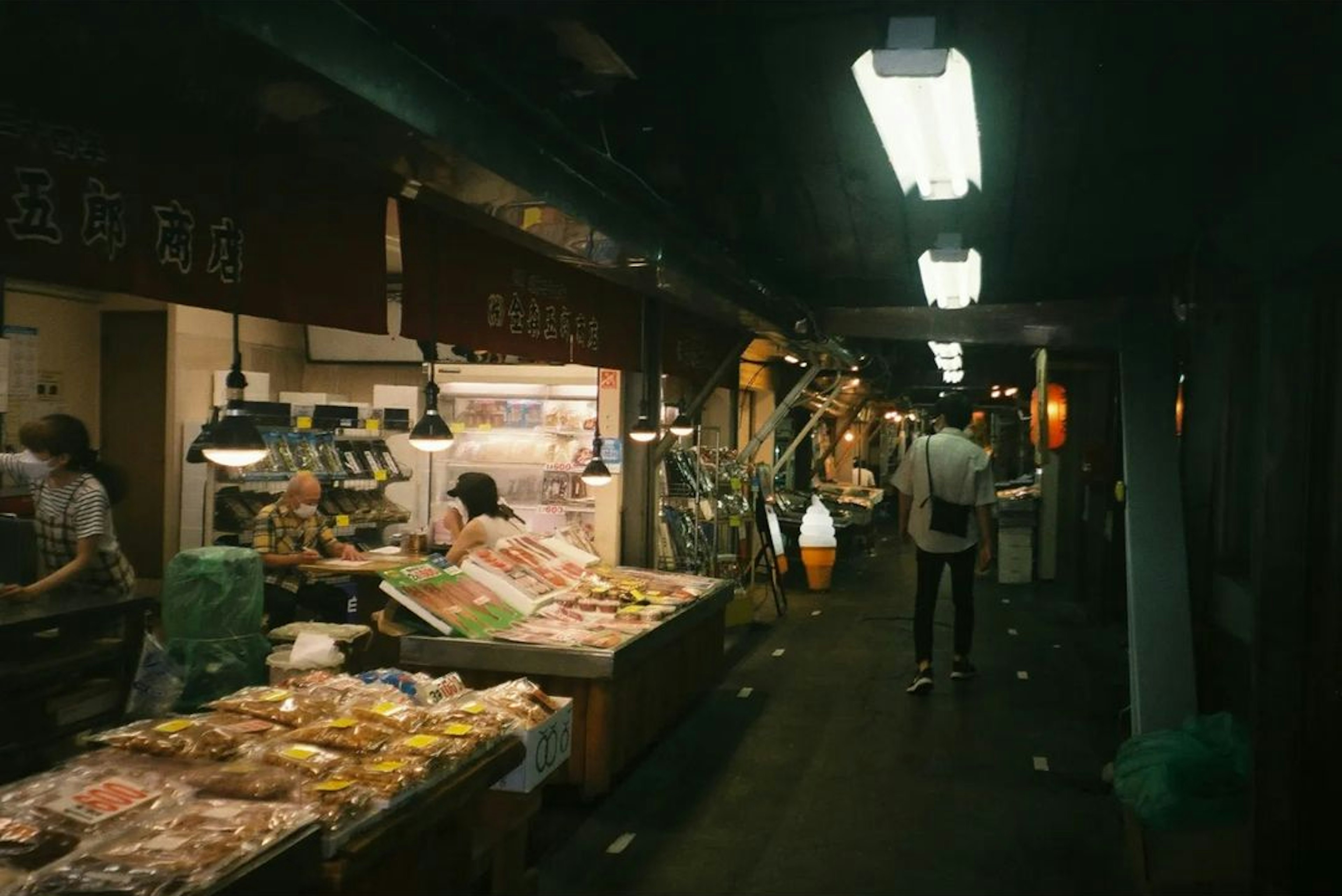 Dimly lit market aisle with food stalls and shoppers