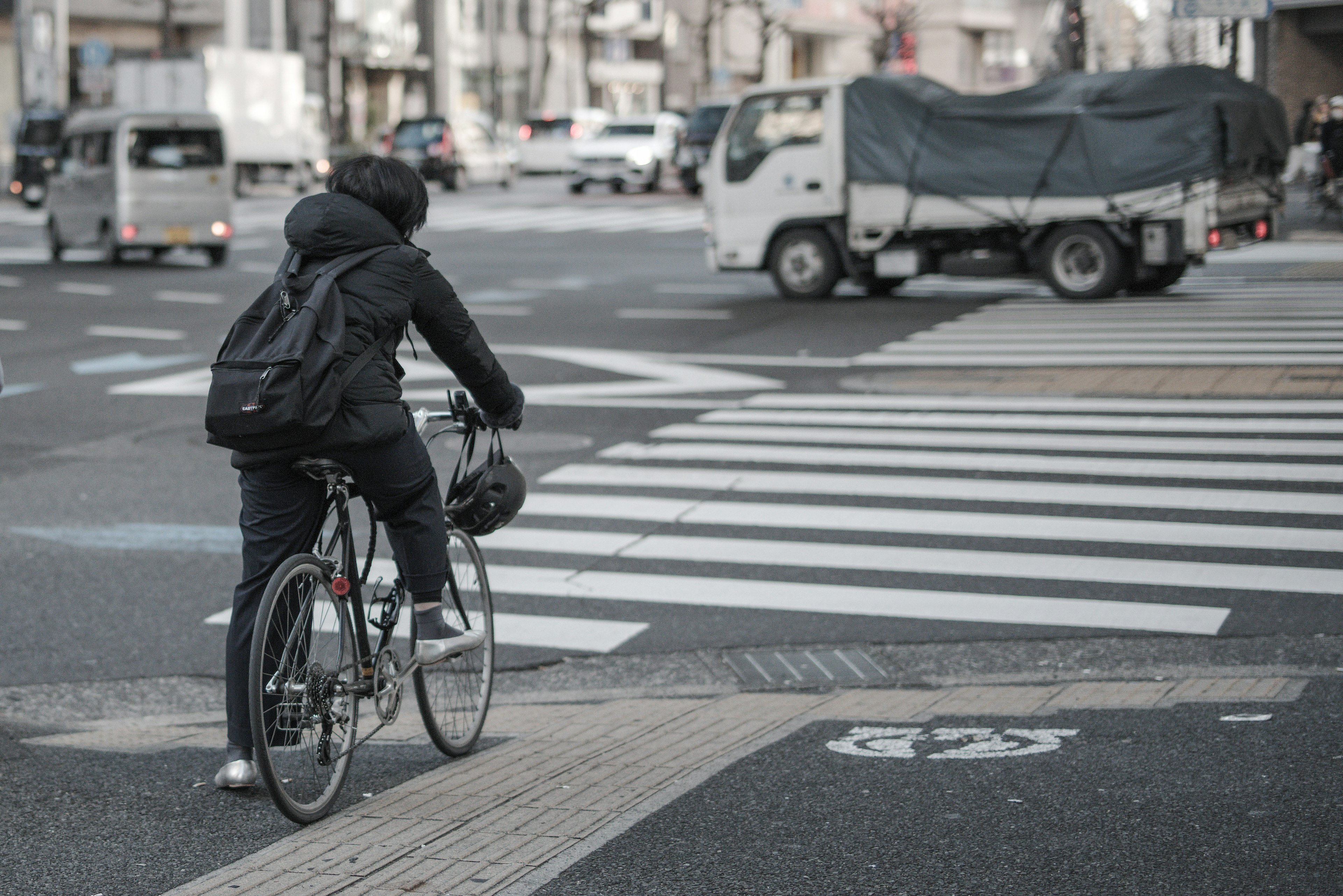 Eine Person auf einem Fahrrad an einem Zebrastreifen mit Fahrzeugen in einer städtischen Umgebung