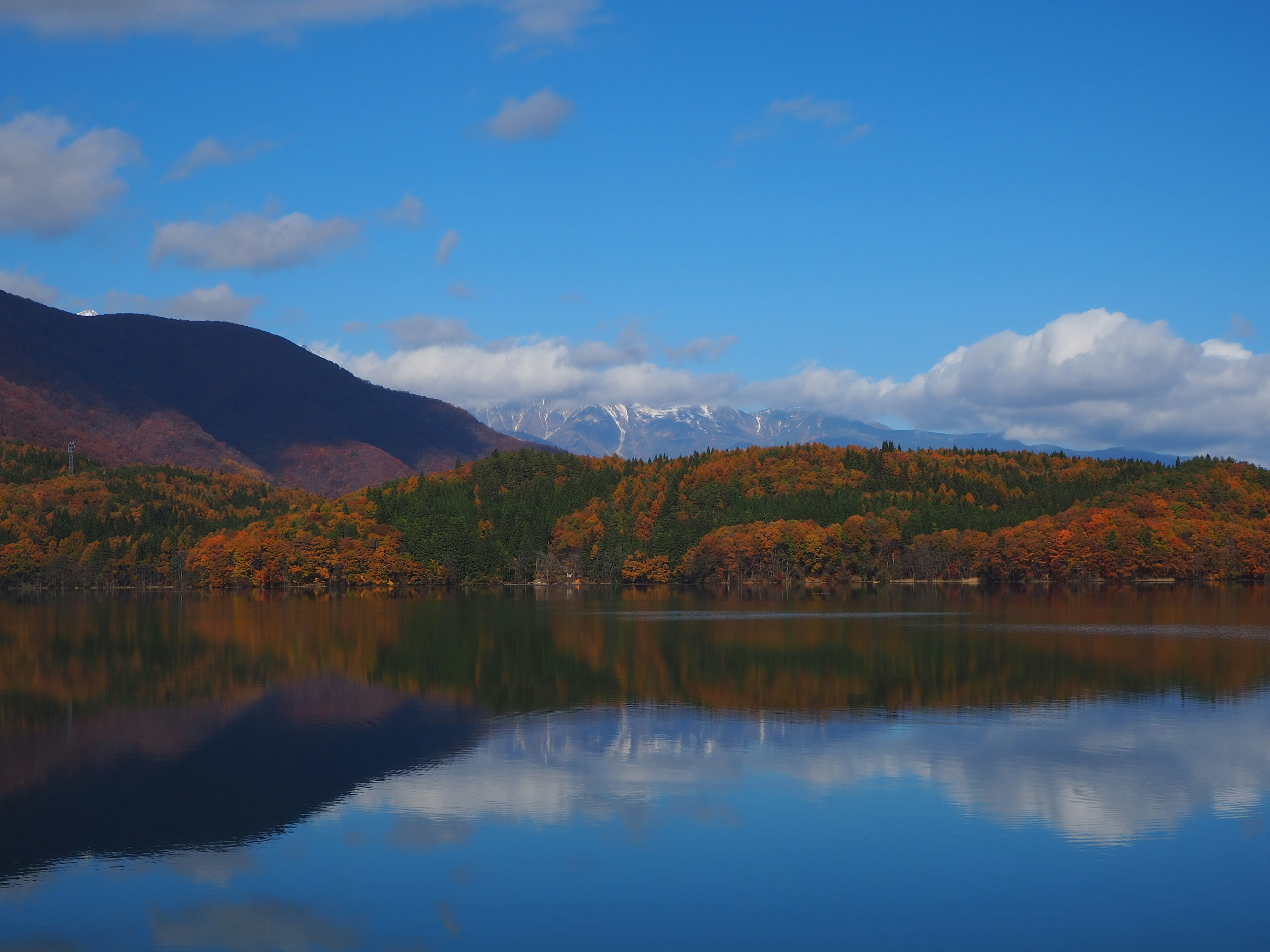 Scenic view of a lake reflecting autumn-colored mountains under a blue sky