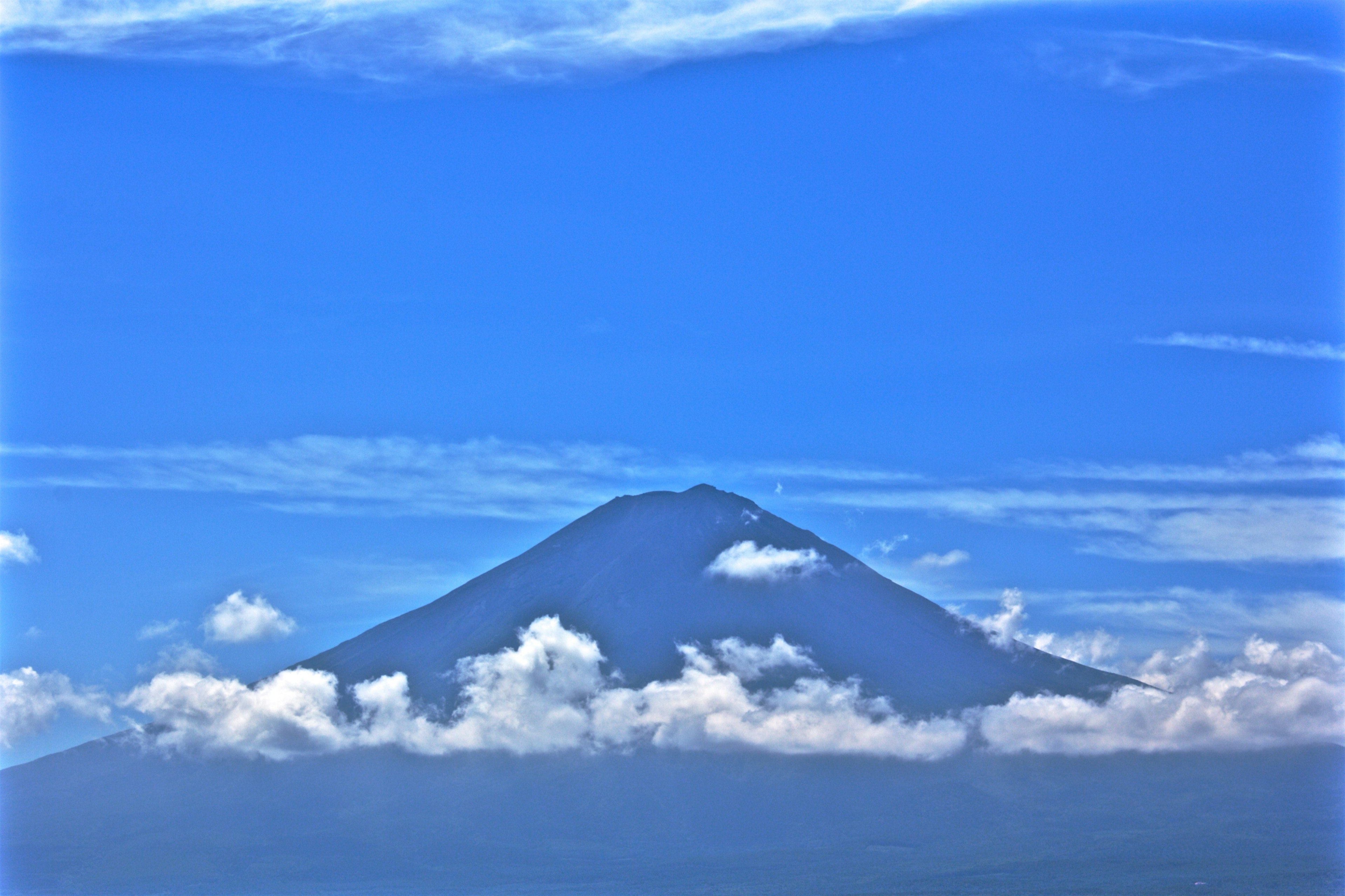 Cima de montaña emergiendo de las nubes bajo un cielo azul