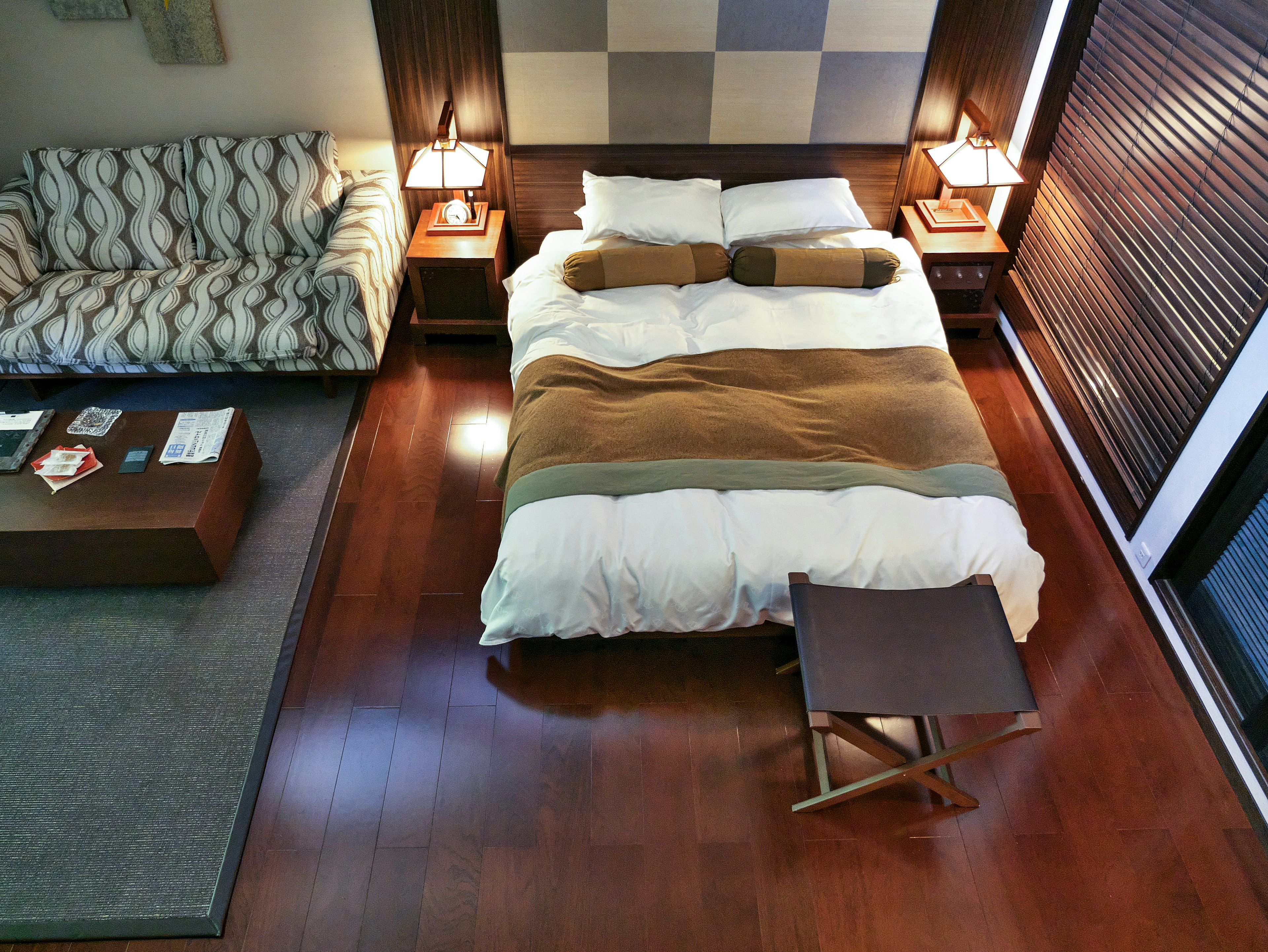 Vue d'ensemble d'une chambre moderne avec un lit avec linge de lit blanc et une couverture marron un canapé et une table sont disposés