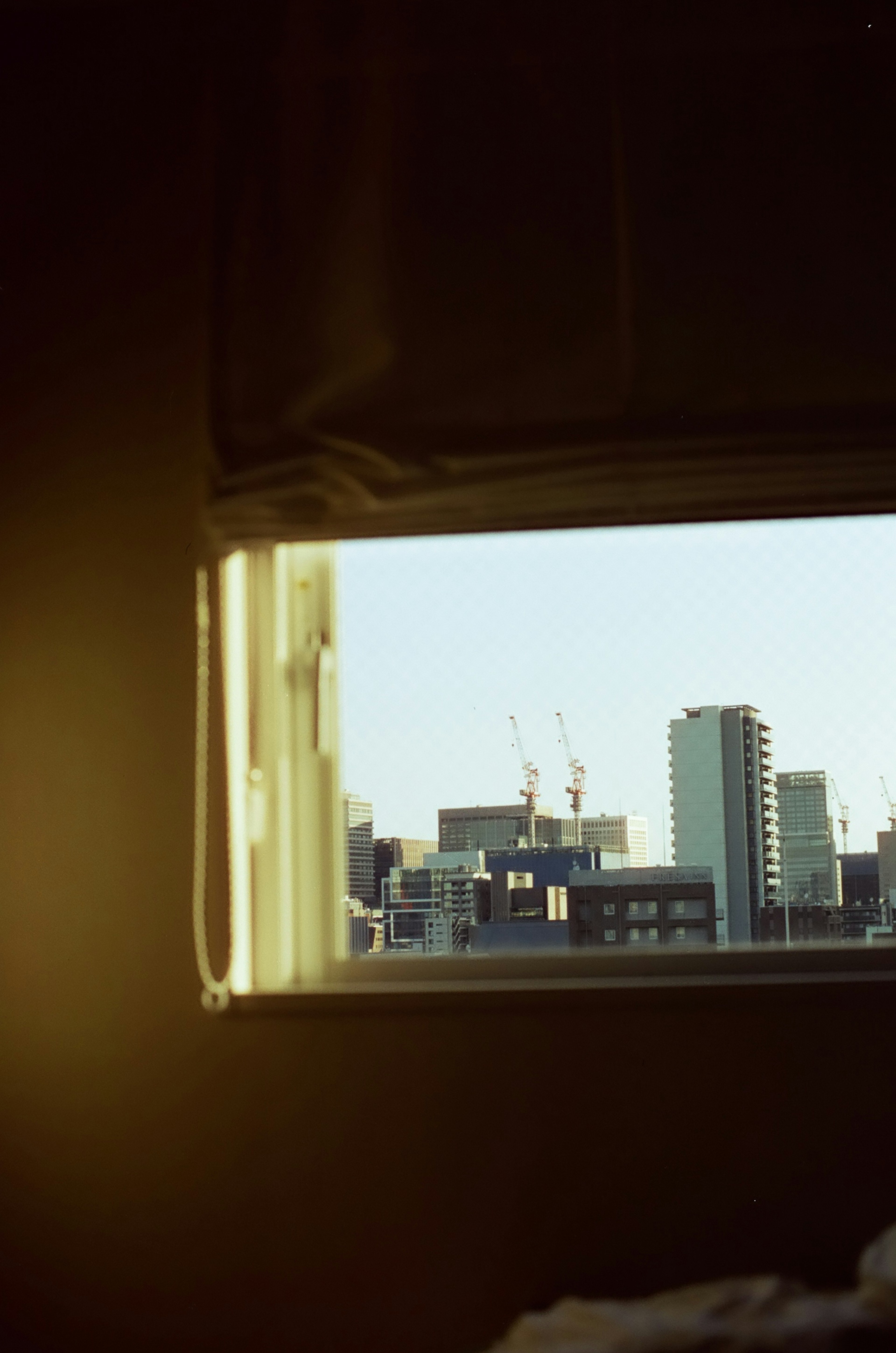 City skyline view through a window featuring buildings and cranes