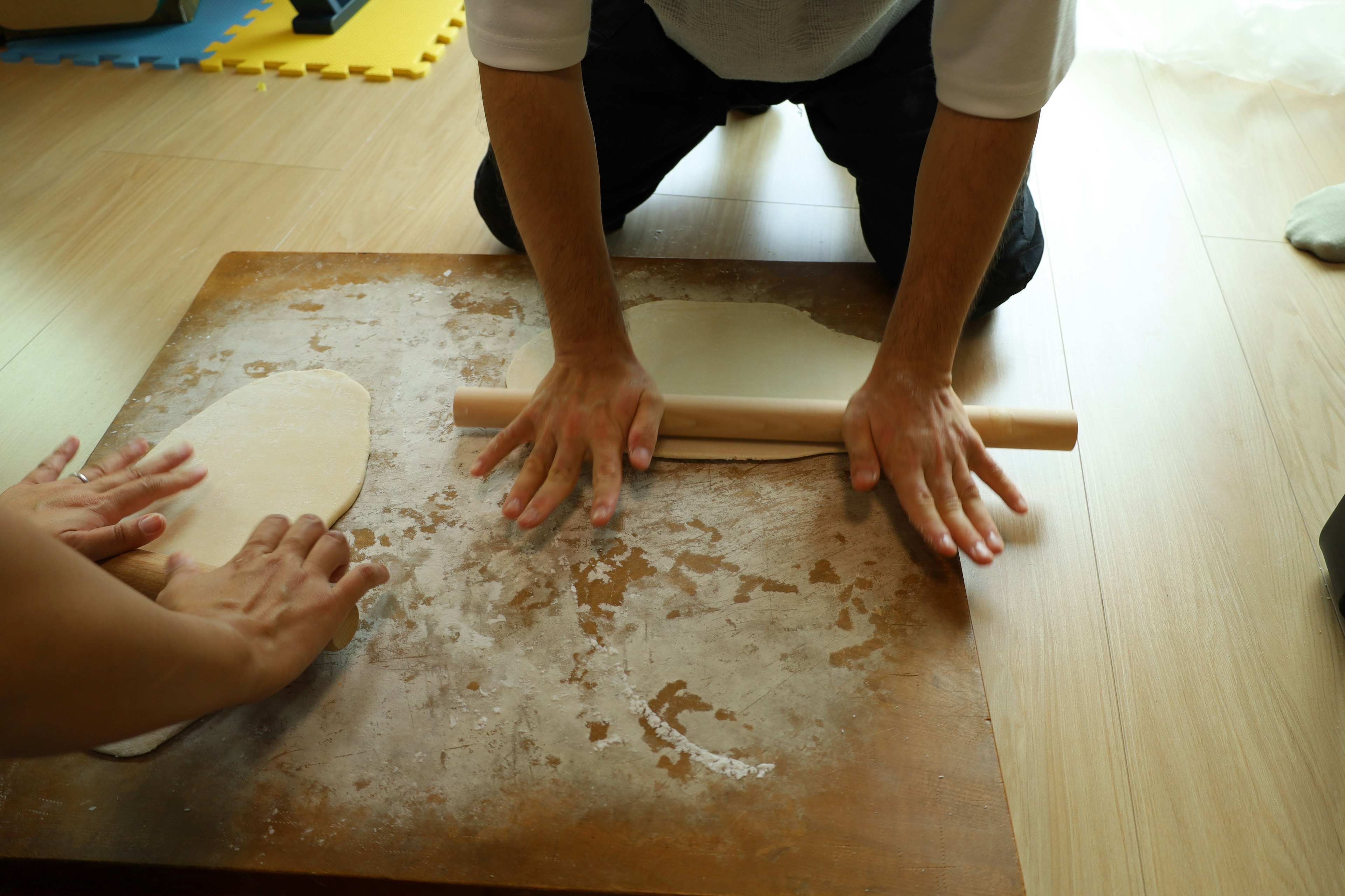 Two hands rolling dough on a flour-covered surface