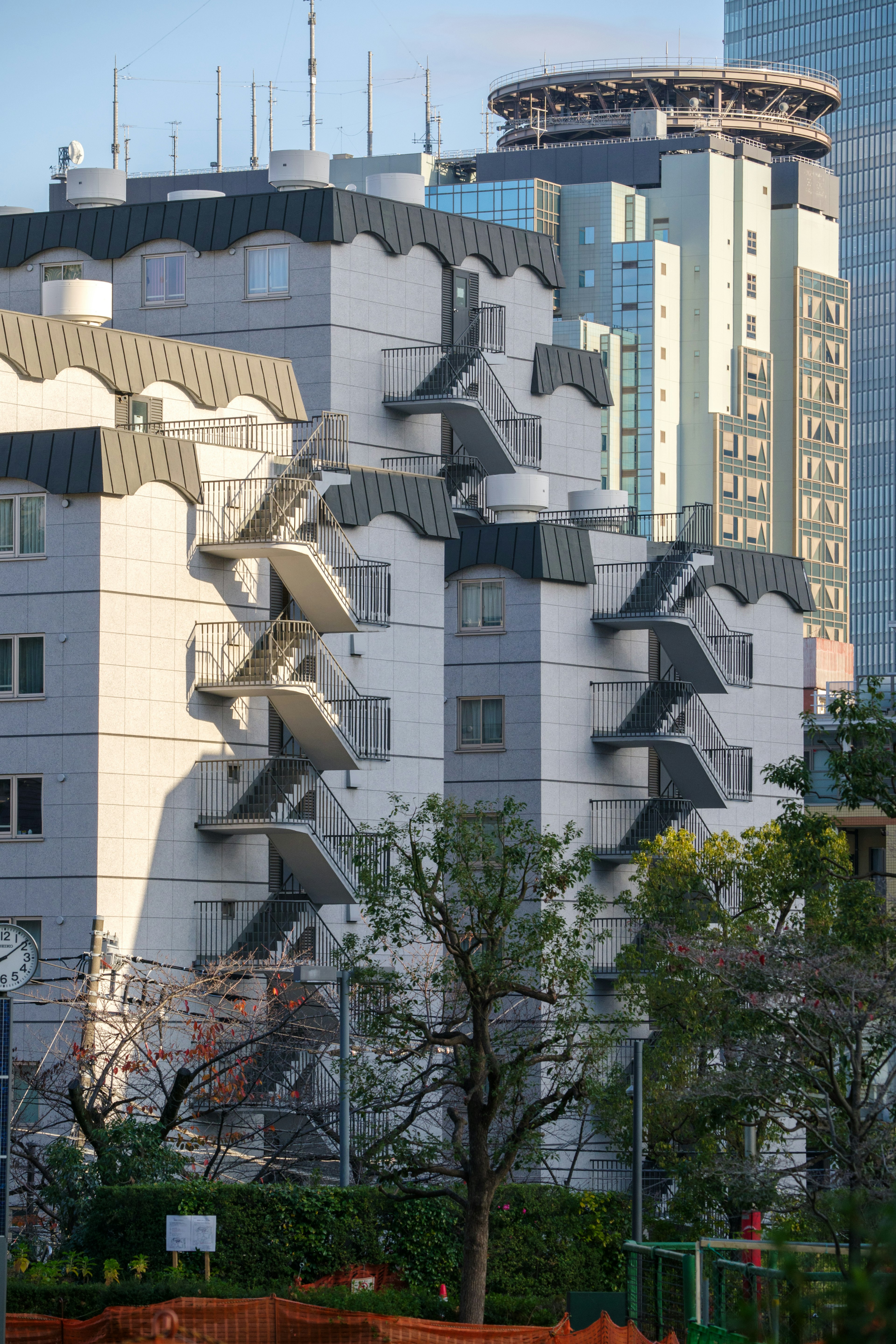 White building with unique architectural features alongside modern skyscrapers and greenery