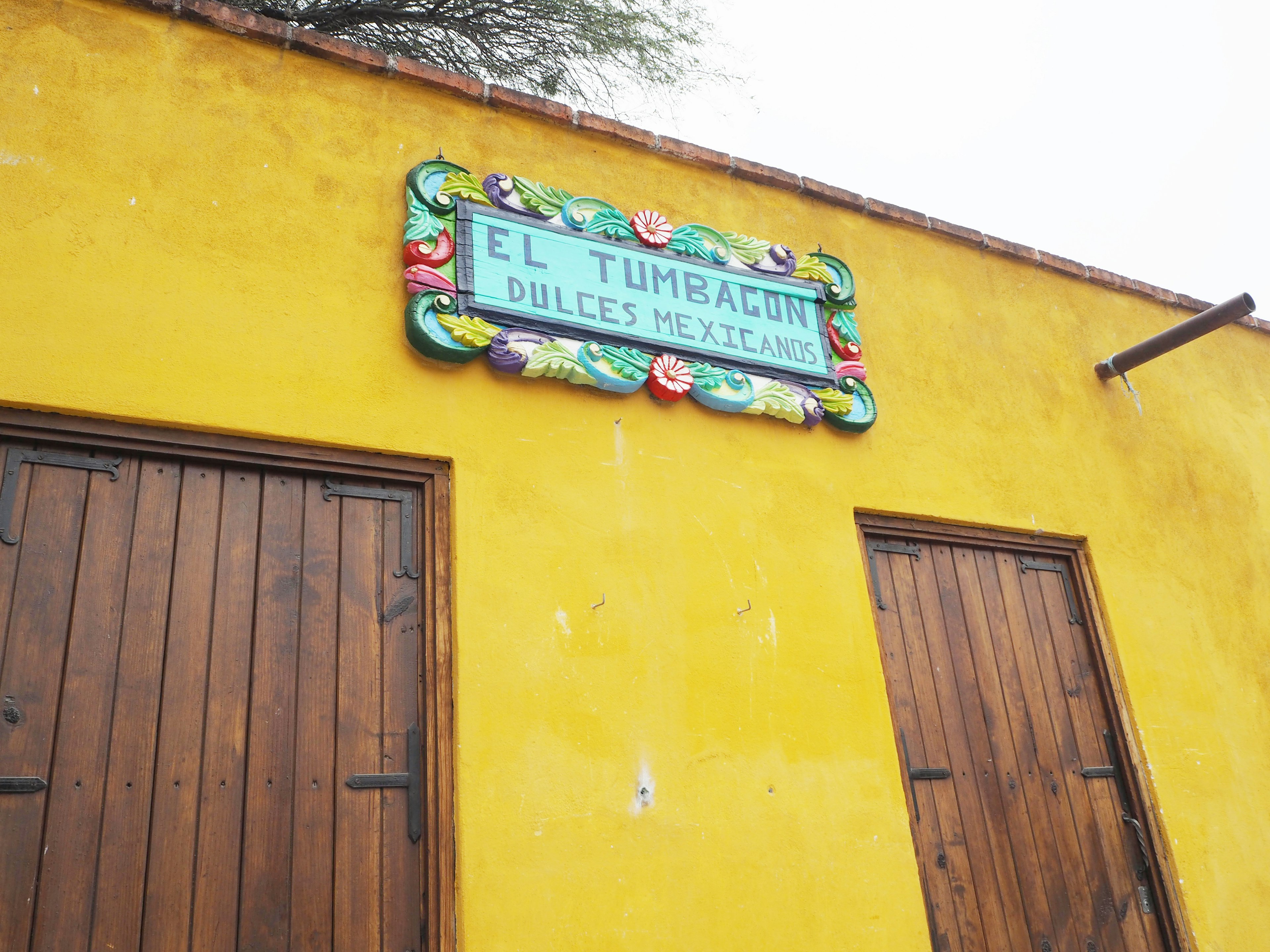 Building with a decorative sign reading El Tumagón Dulces Mexicanos on a yellow wall