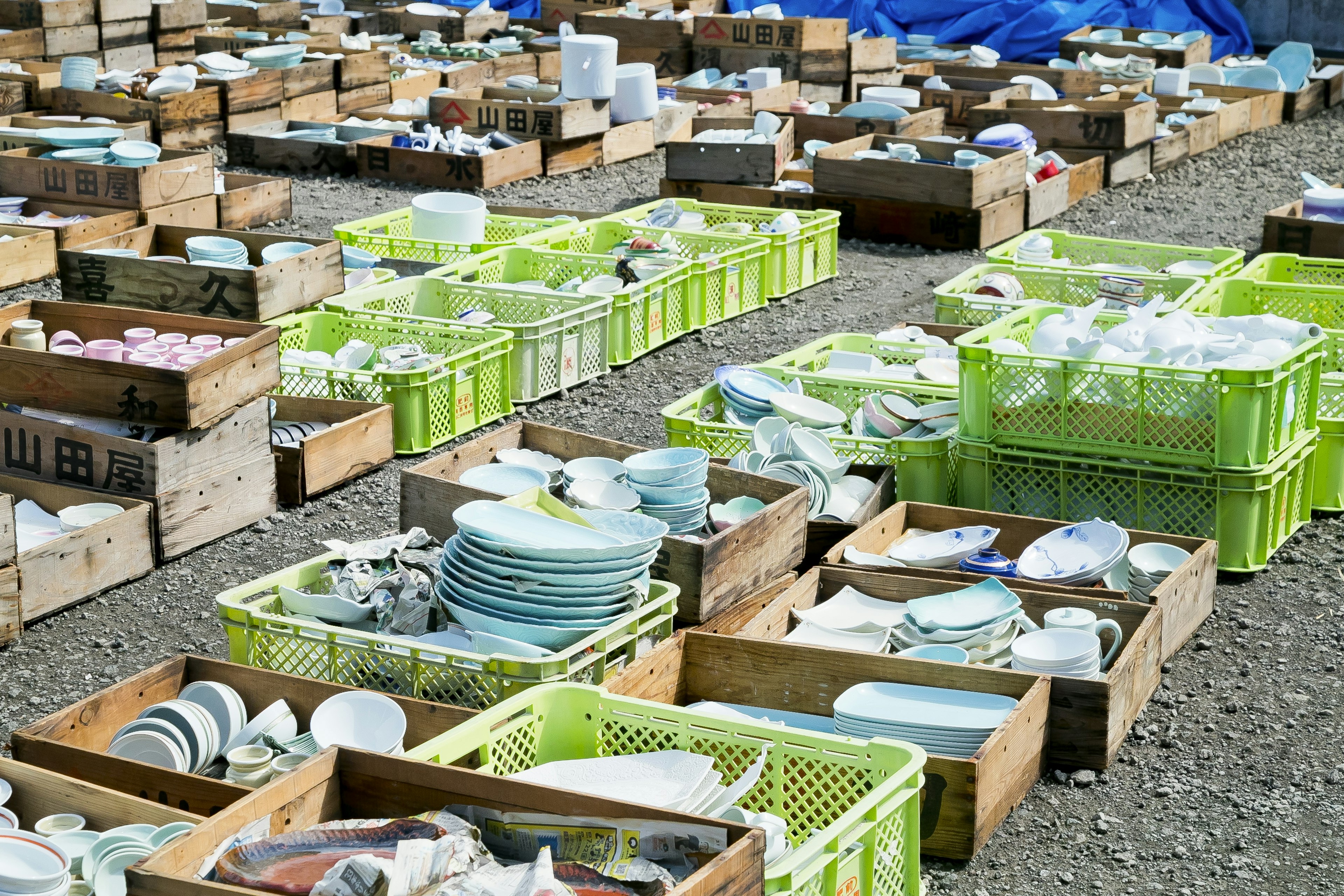 A collection of dishware organized in wooden boxes and green crates