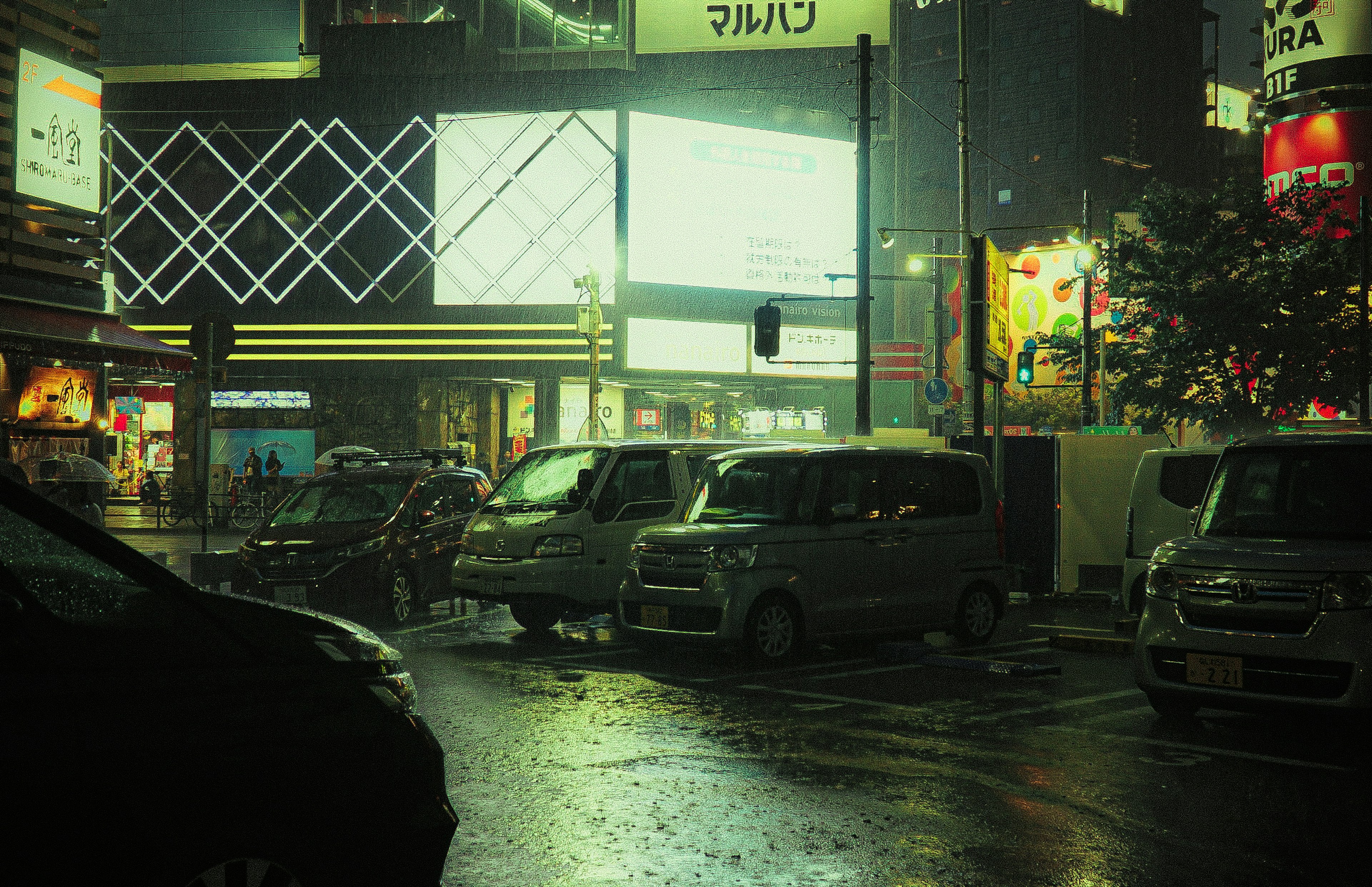 Cars parked on a rainy street corner with neon signs