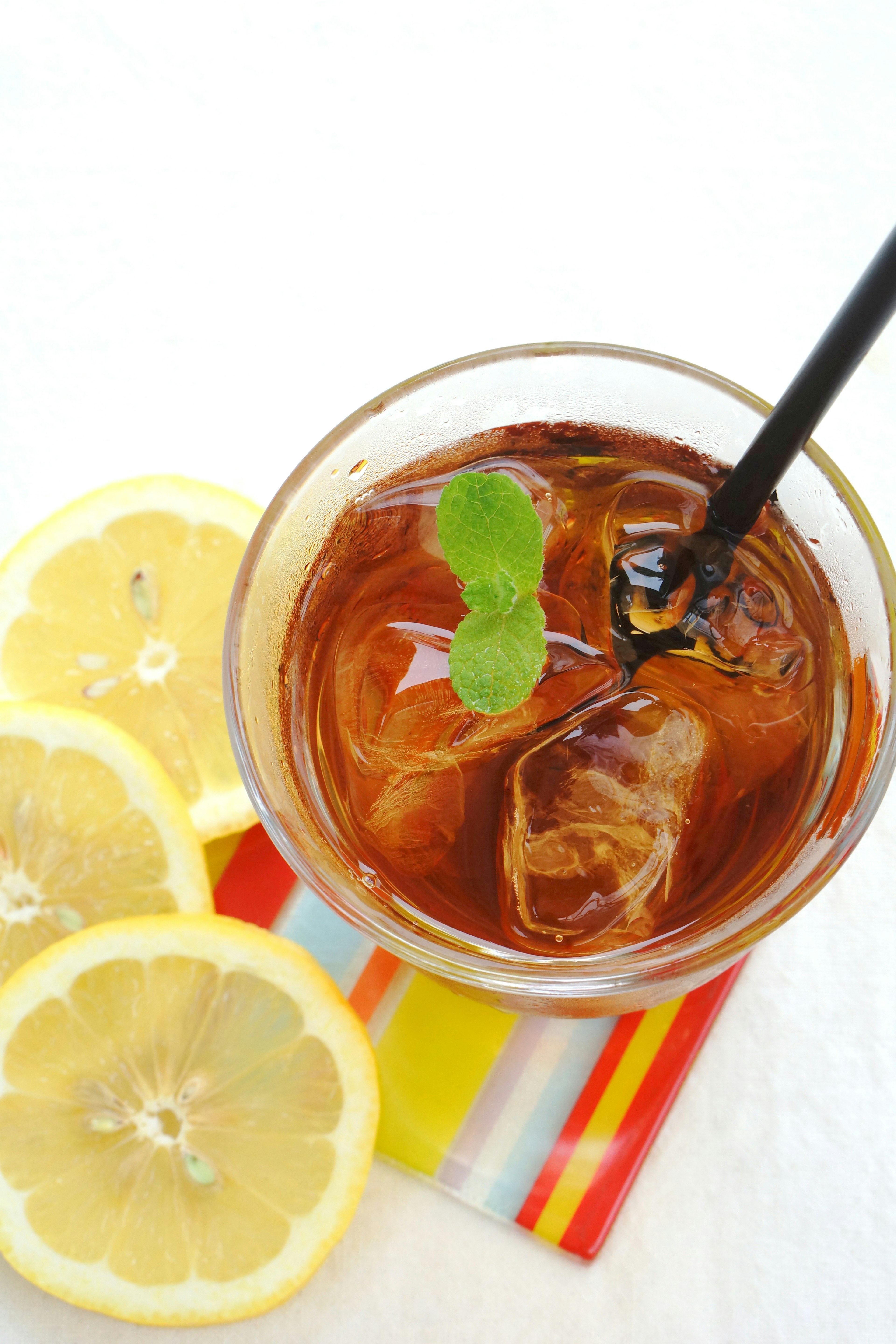 Image of a glass of iced tea with ice cubes and lemon slices on a bright background