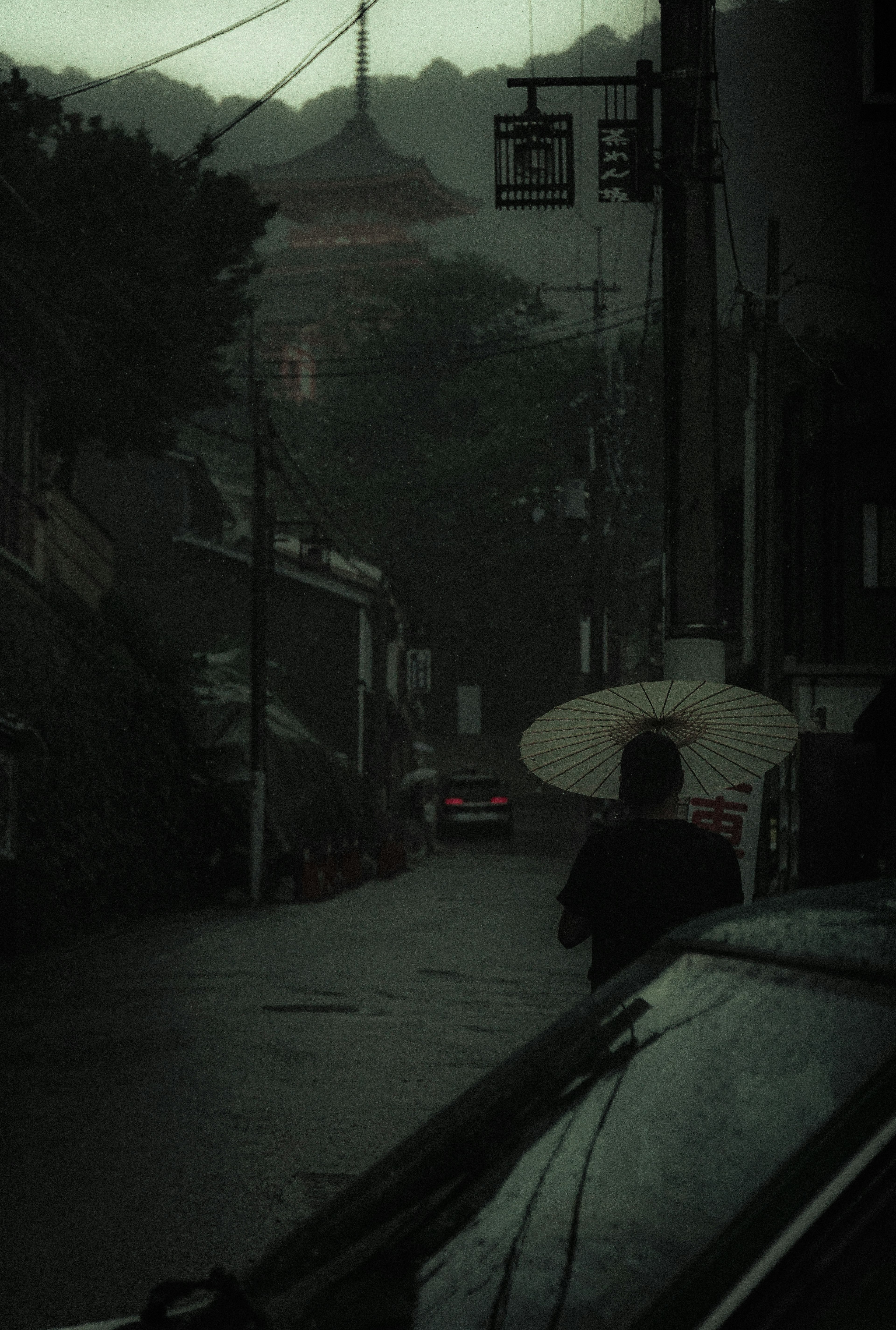 Eine schattenhafte Figur, die mit einem Regenschirm auf einer schwach beleuchteten Straße geht