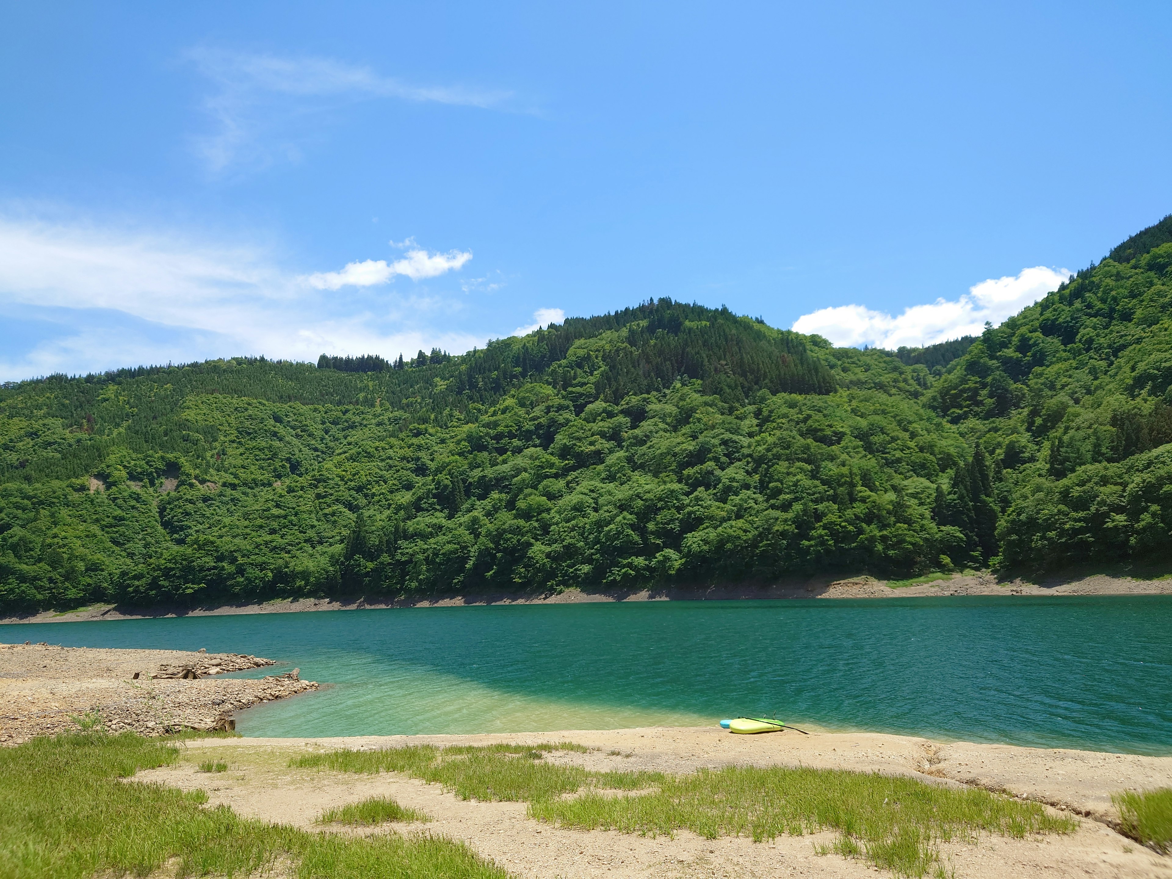 Ruhiger See umgeben von grünen Bergen und blauem Himmel