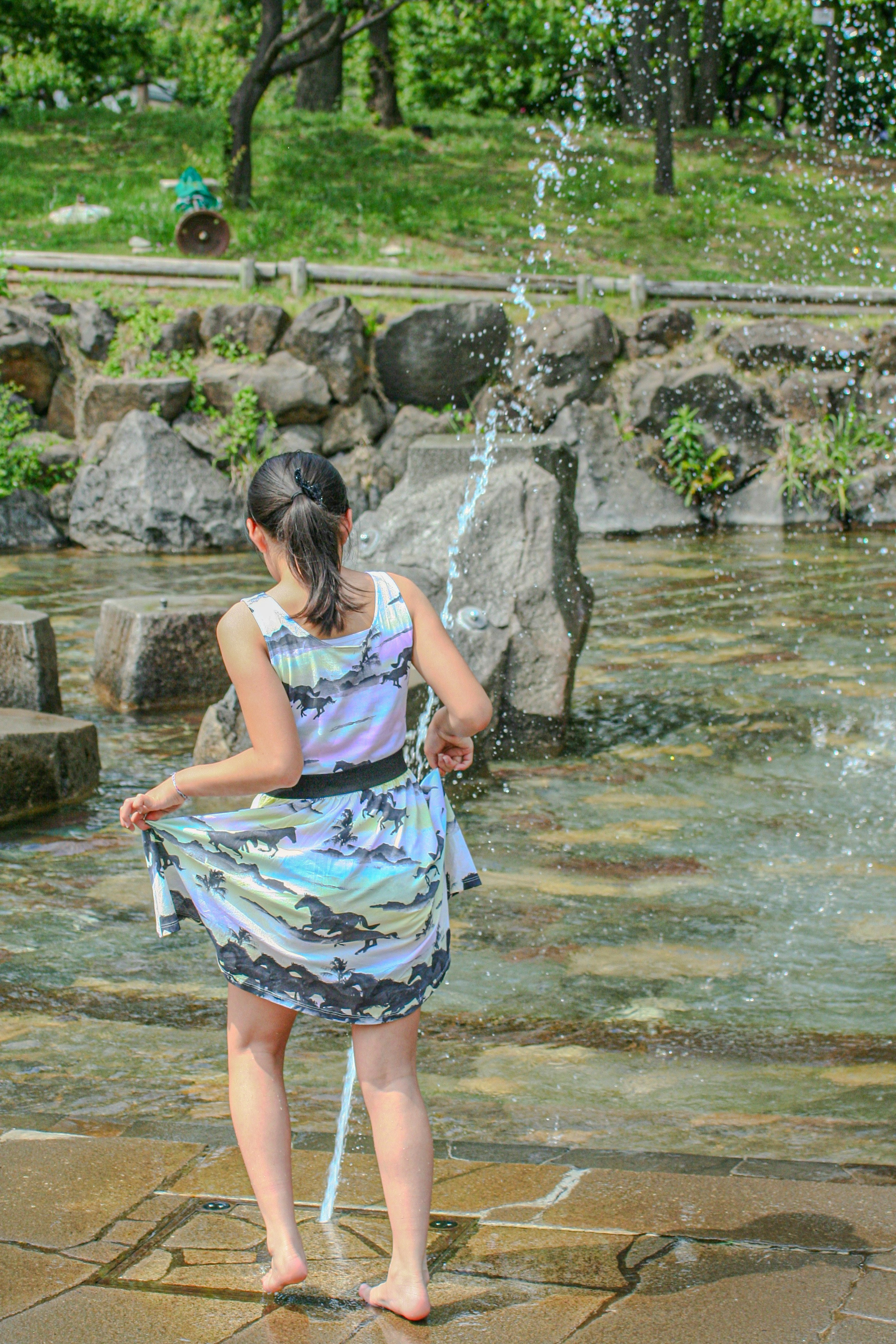 水の噴水の近くで遊ぶ女性の後ろ姿 緑の公園の背景