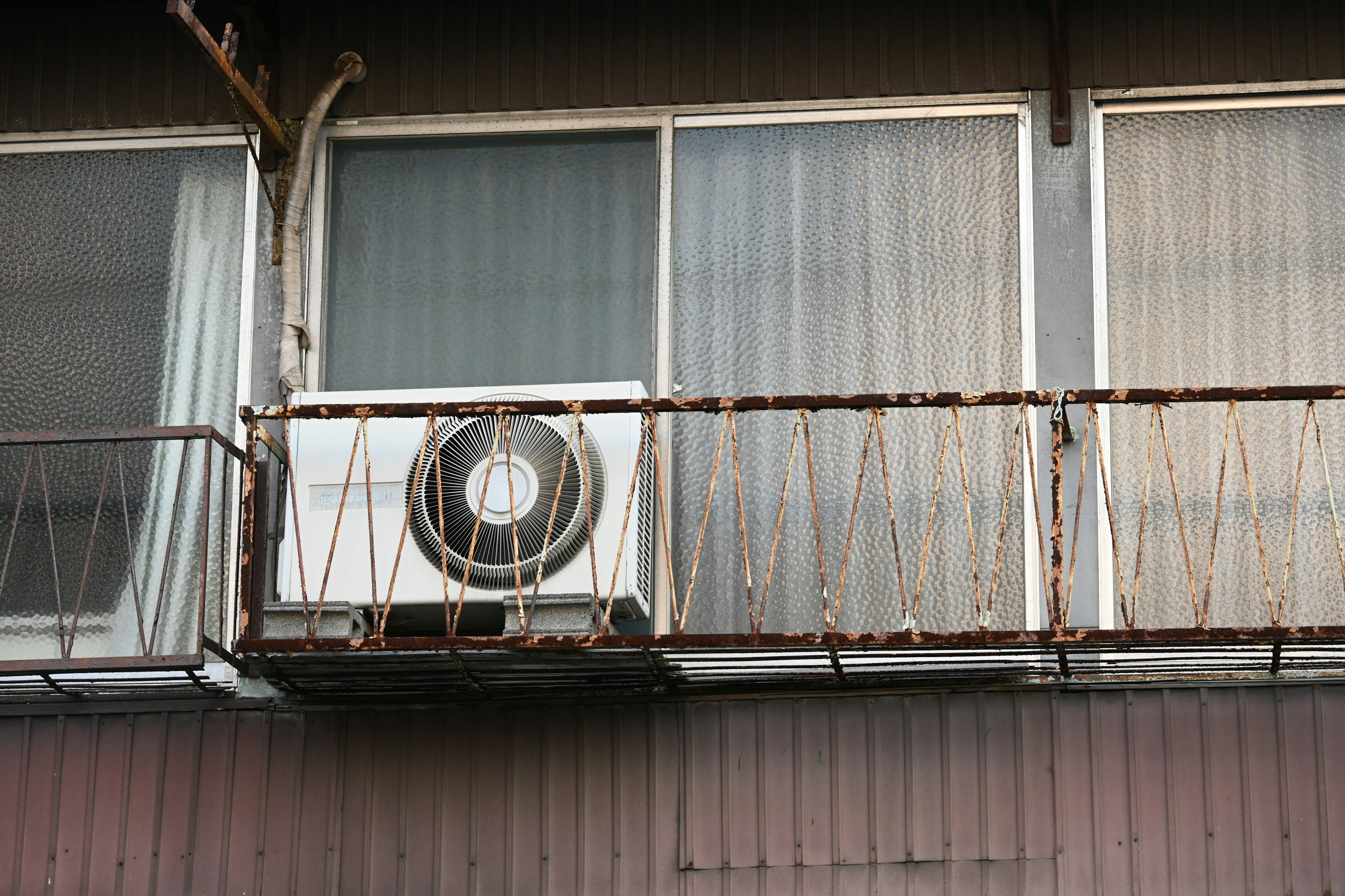 Air conditioning unit on a balcony of an old apartment with rusted railing