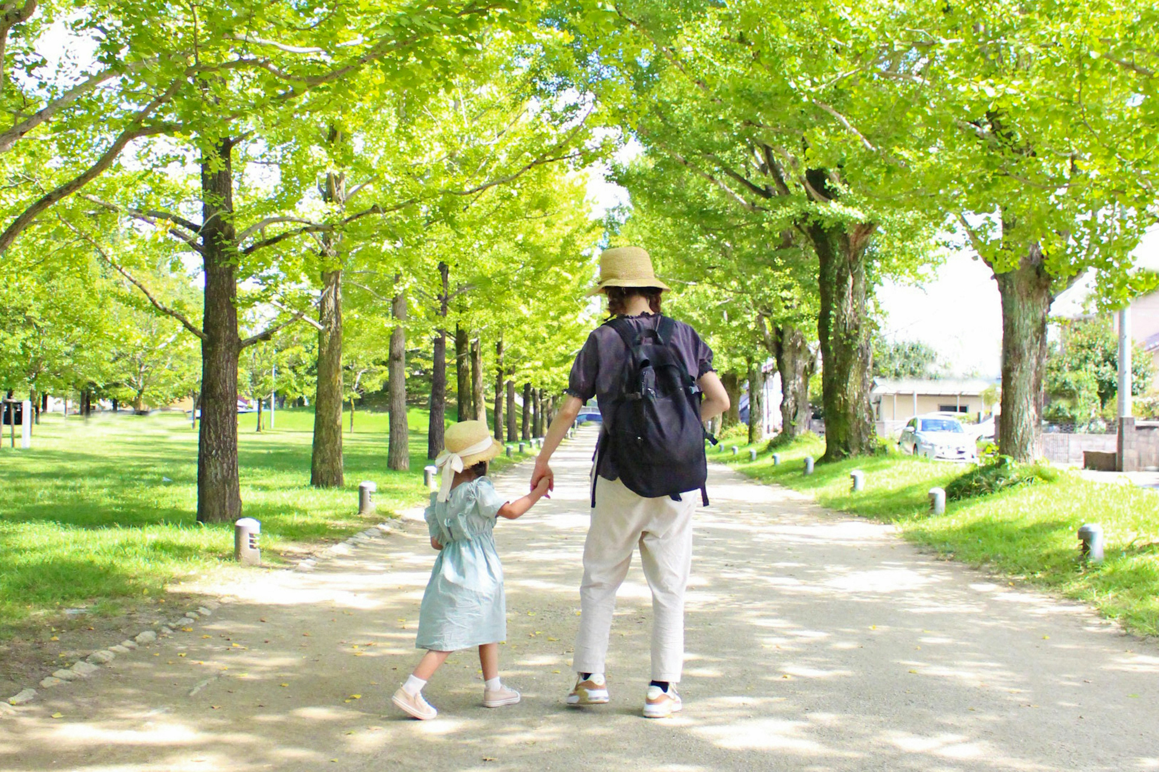 Parent et enfant marchant main dans la main sur un chemin bordé d'arbres