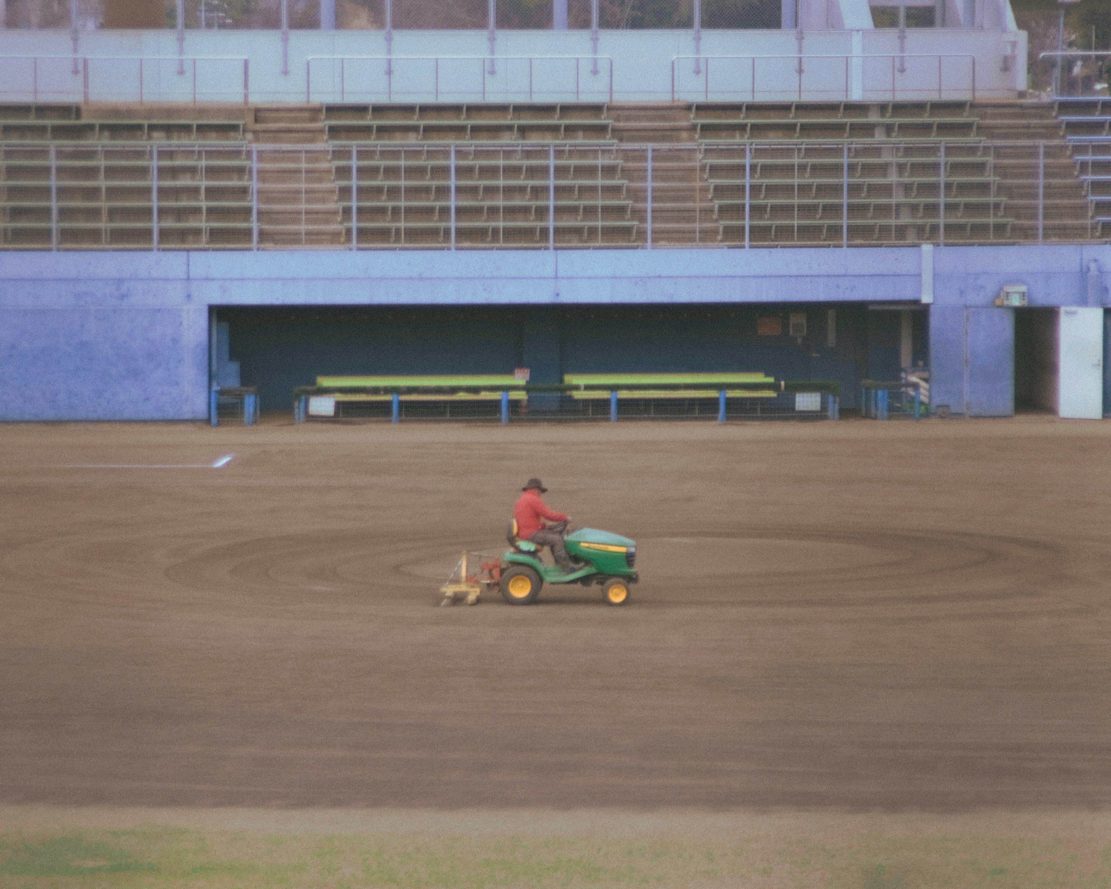 Traktor hijau dengan pekerja berpakaian merah merawat lapangan rumput