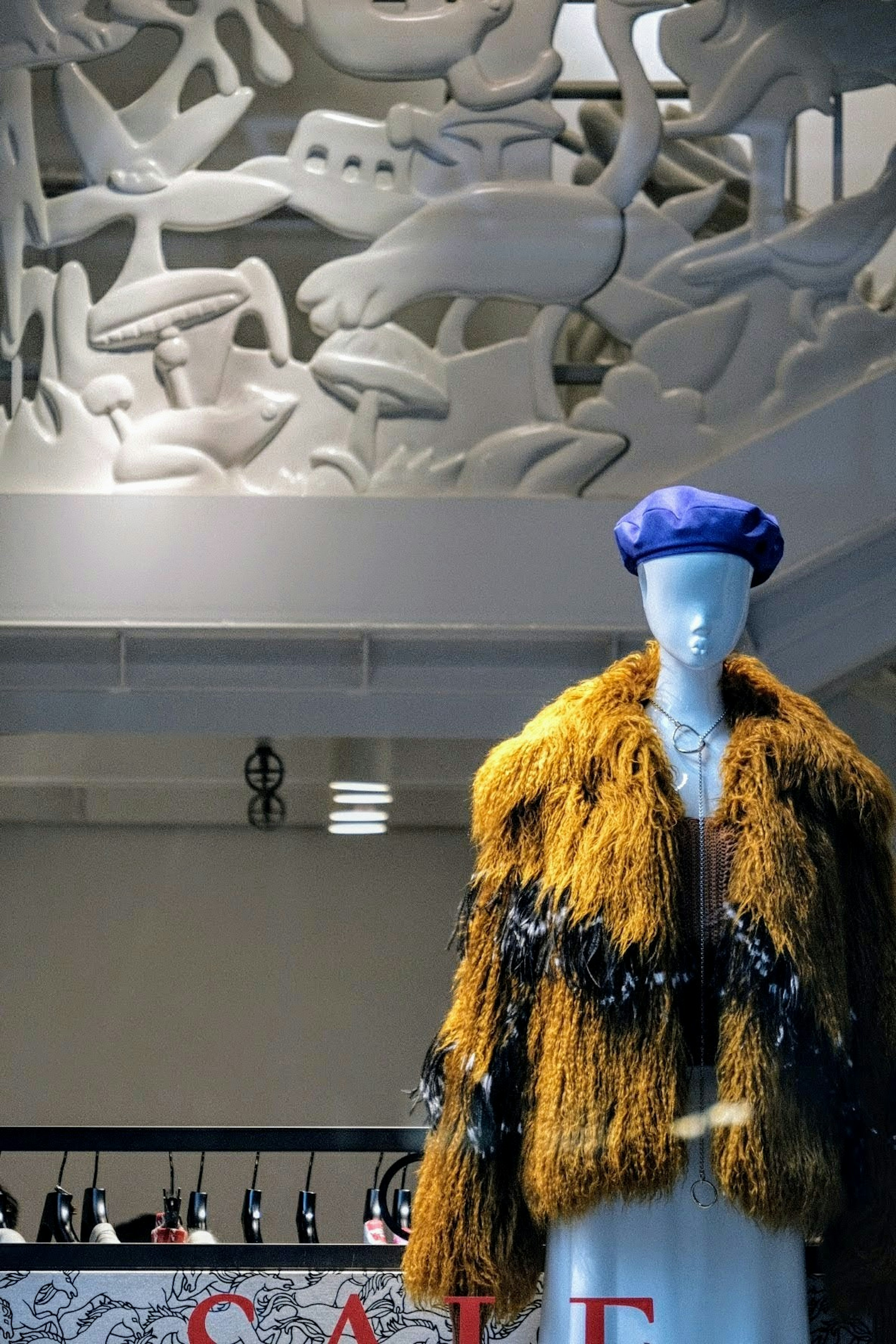 Mannequin présentant un manteau en fourrure jaune et un chapeau bleu dans une vitrine de mode