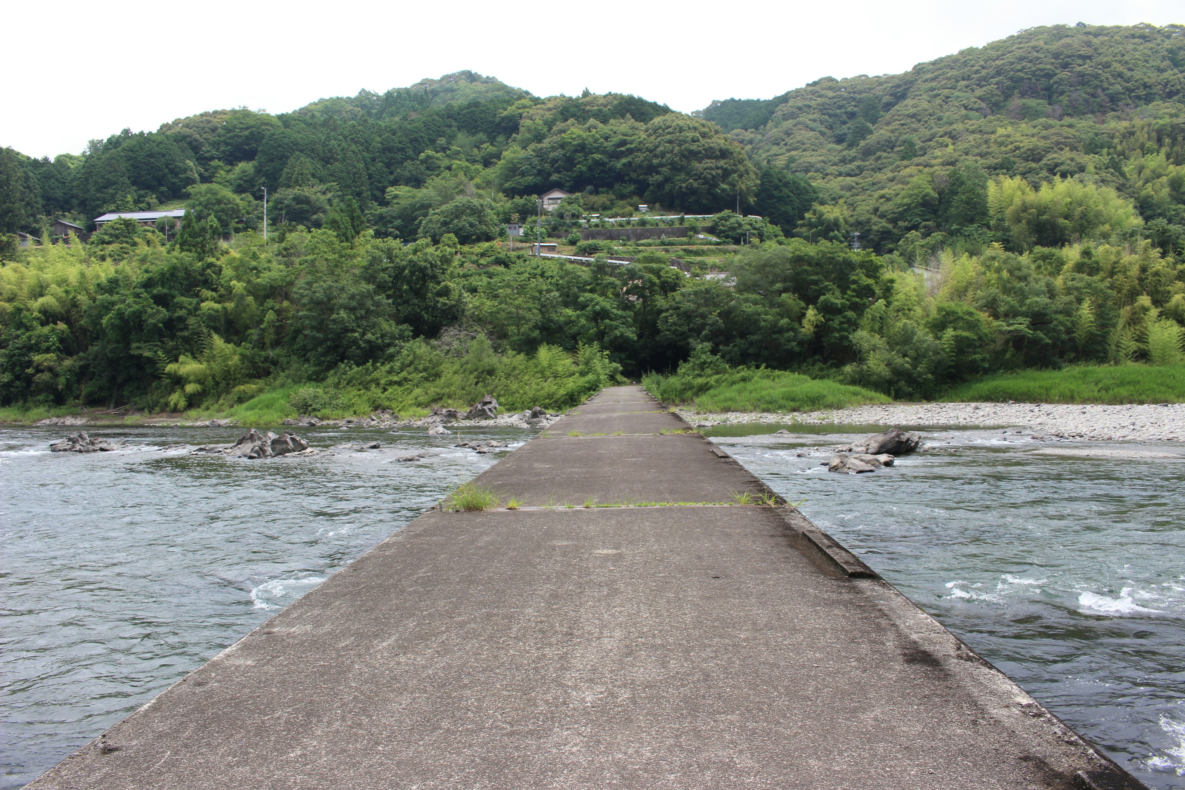 Jalan beton yang melintasi sungai dikelilingi bukit hijau