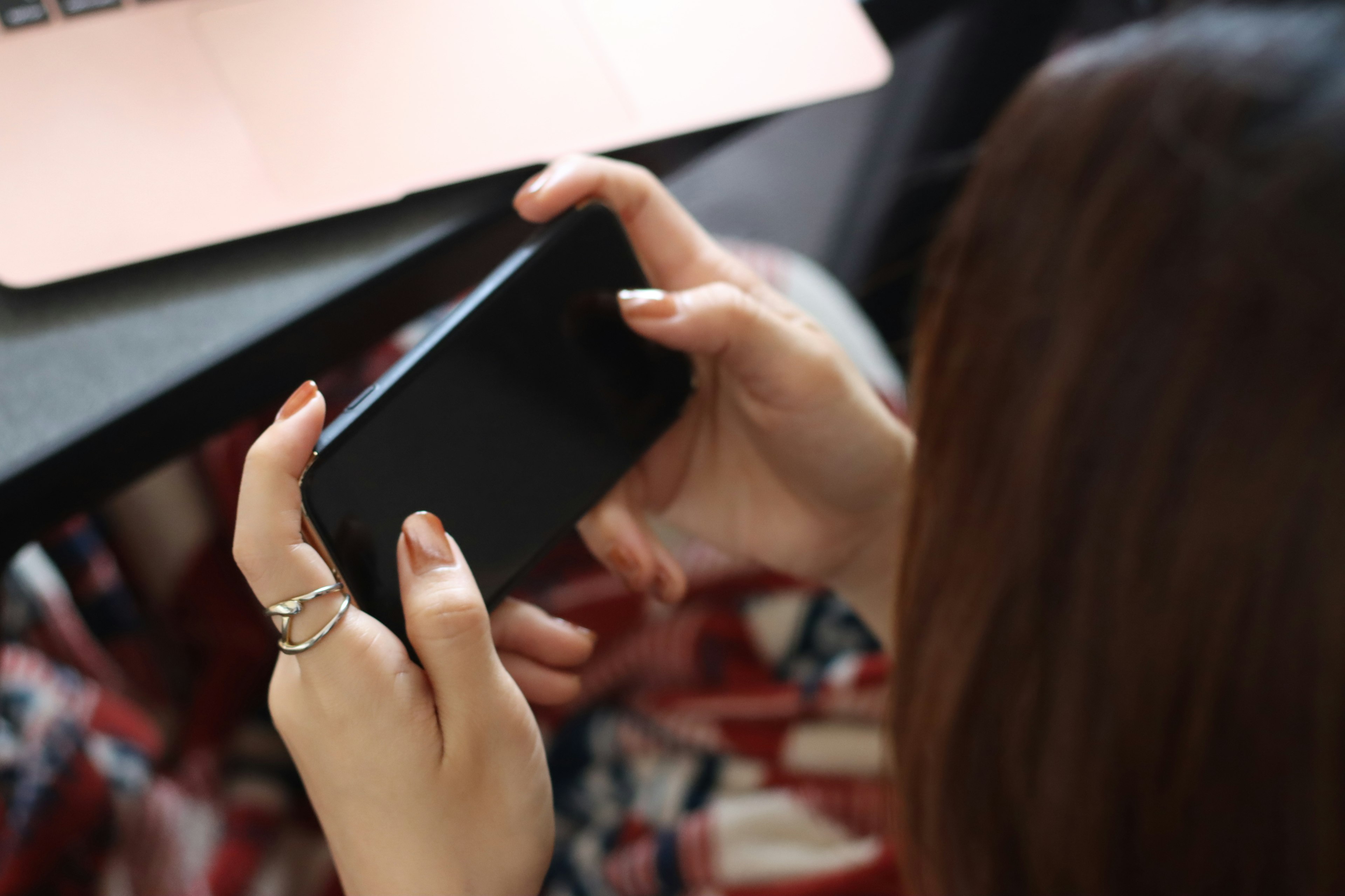 A woman holding a smartphone with a laptop in the background