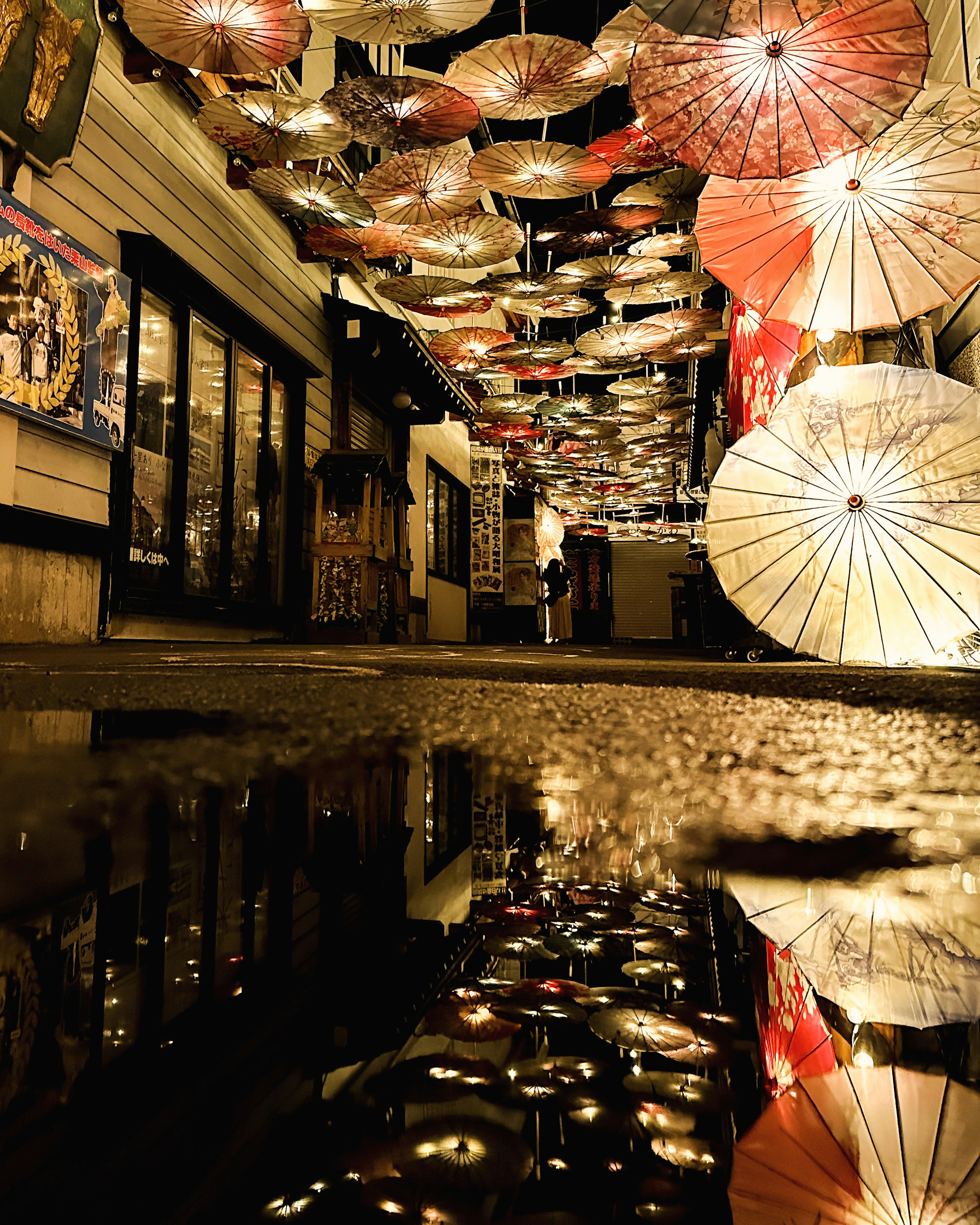 Night alley adorned with hanging umbrellas reflecting light on wet ground