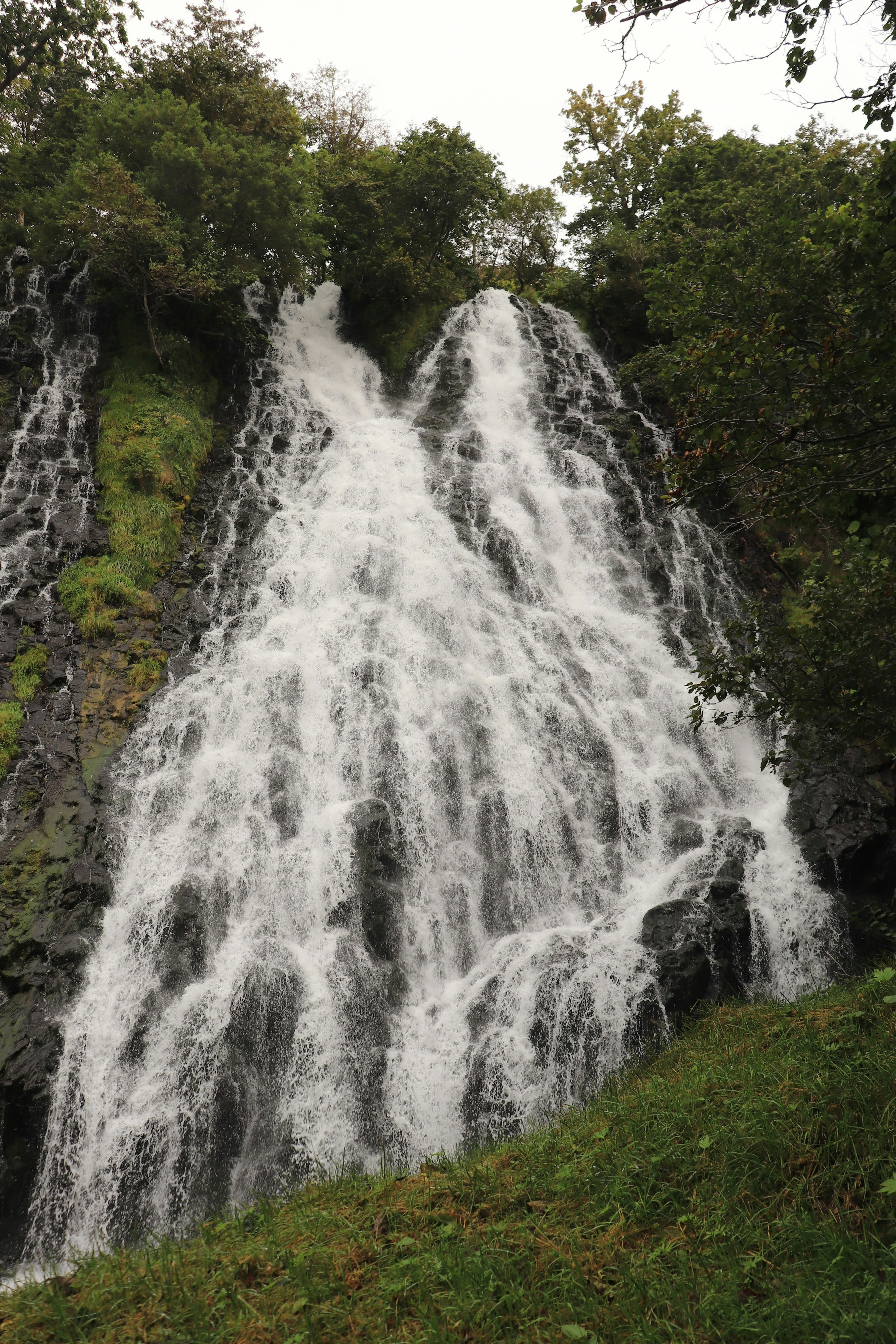 Air terjun indah mengalir di lereng berbatu dikelilingi oleh tanaman hijau