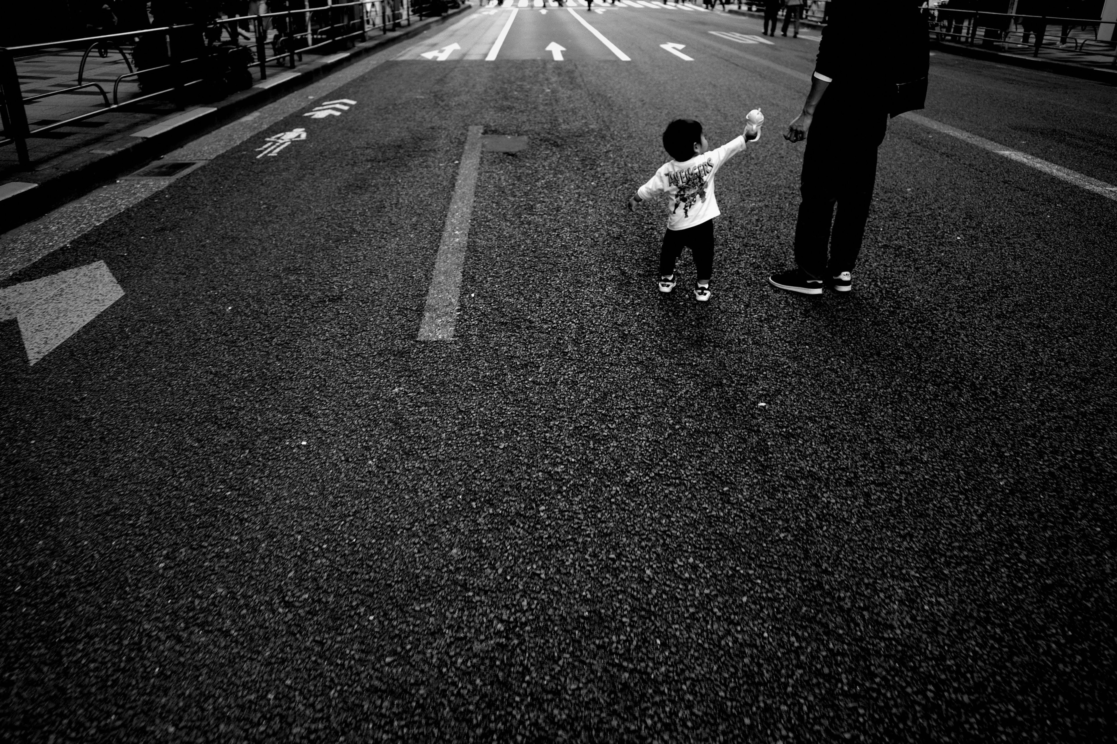 Enfant tenant la main d'un adulte marchant sur une rue en noir et blanc