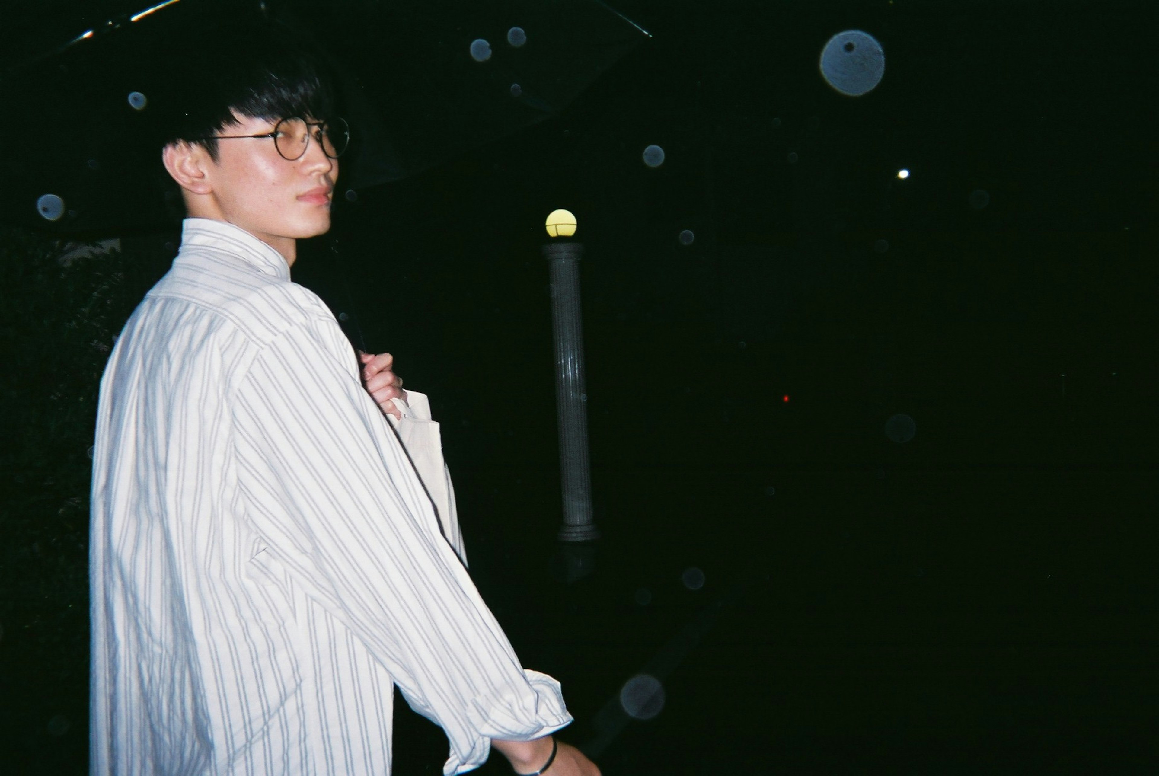 A young man in a white striped shirt turns back against a dark background