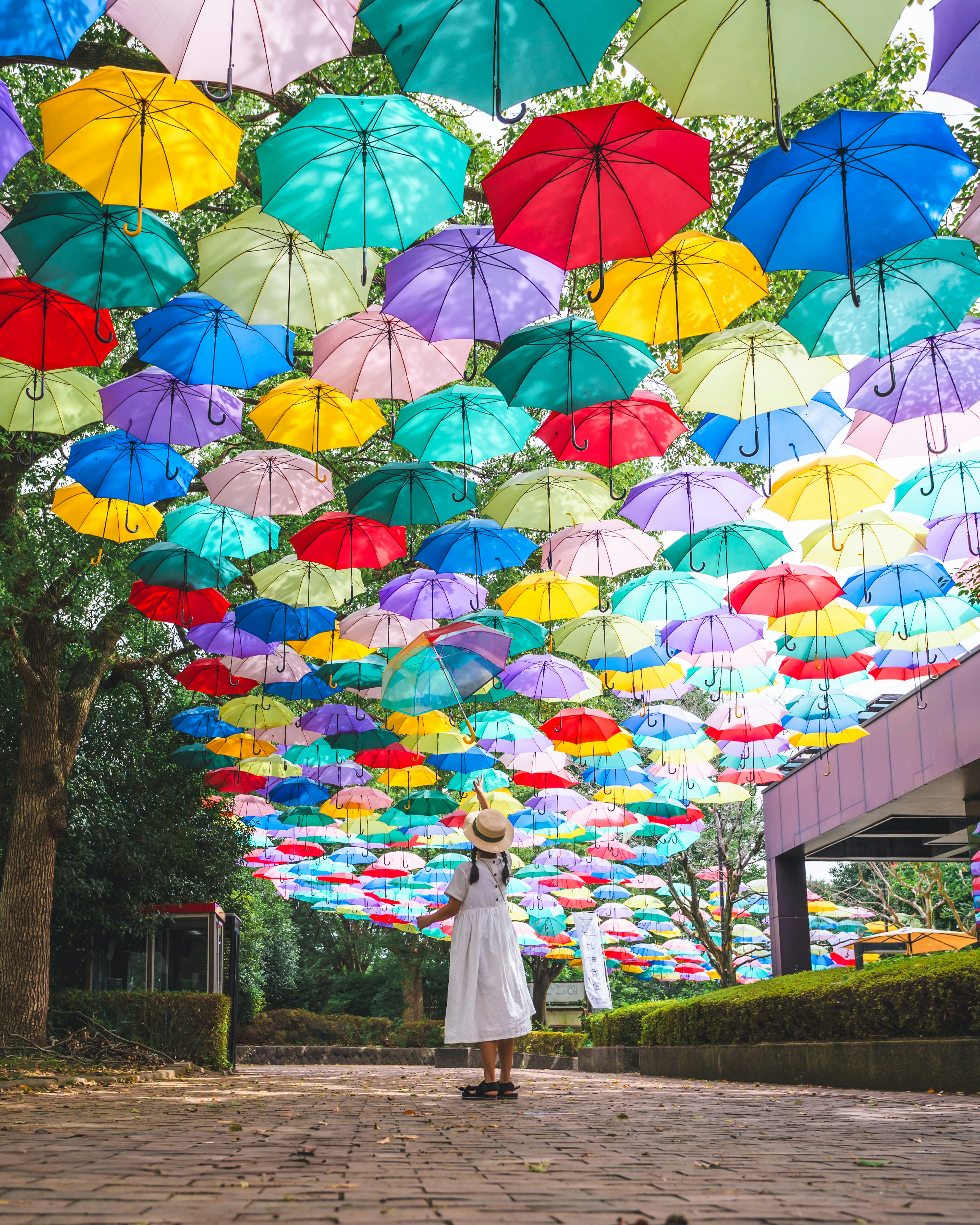 Una mujer de pie bajo una instalación de paraguas coloridos en un parque