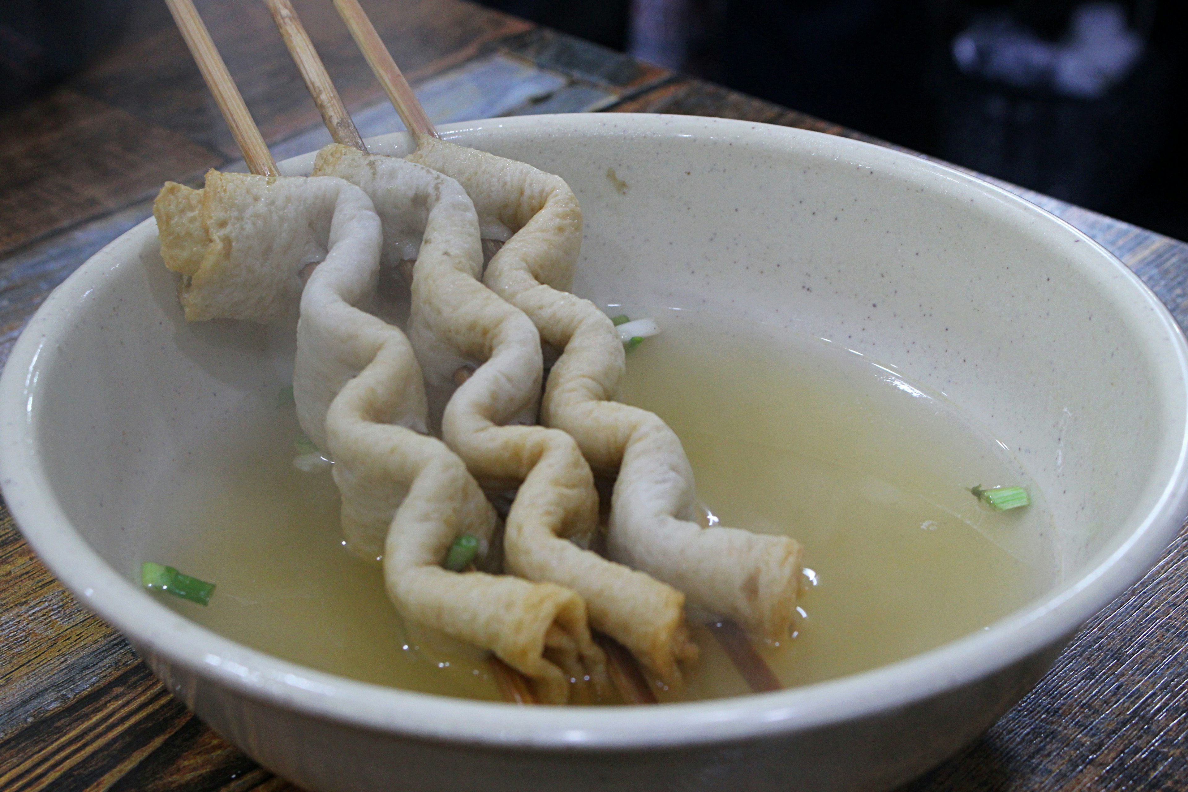 Wavy dumplings being lifted with chopsticks from a bowl of broth