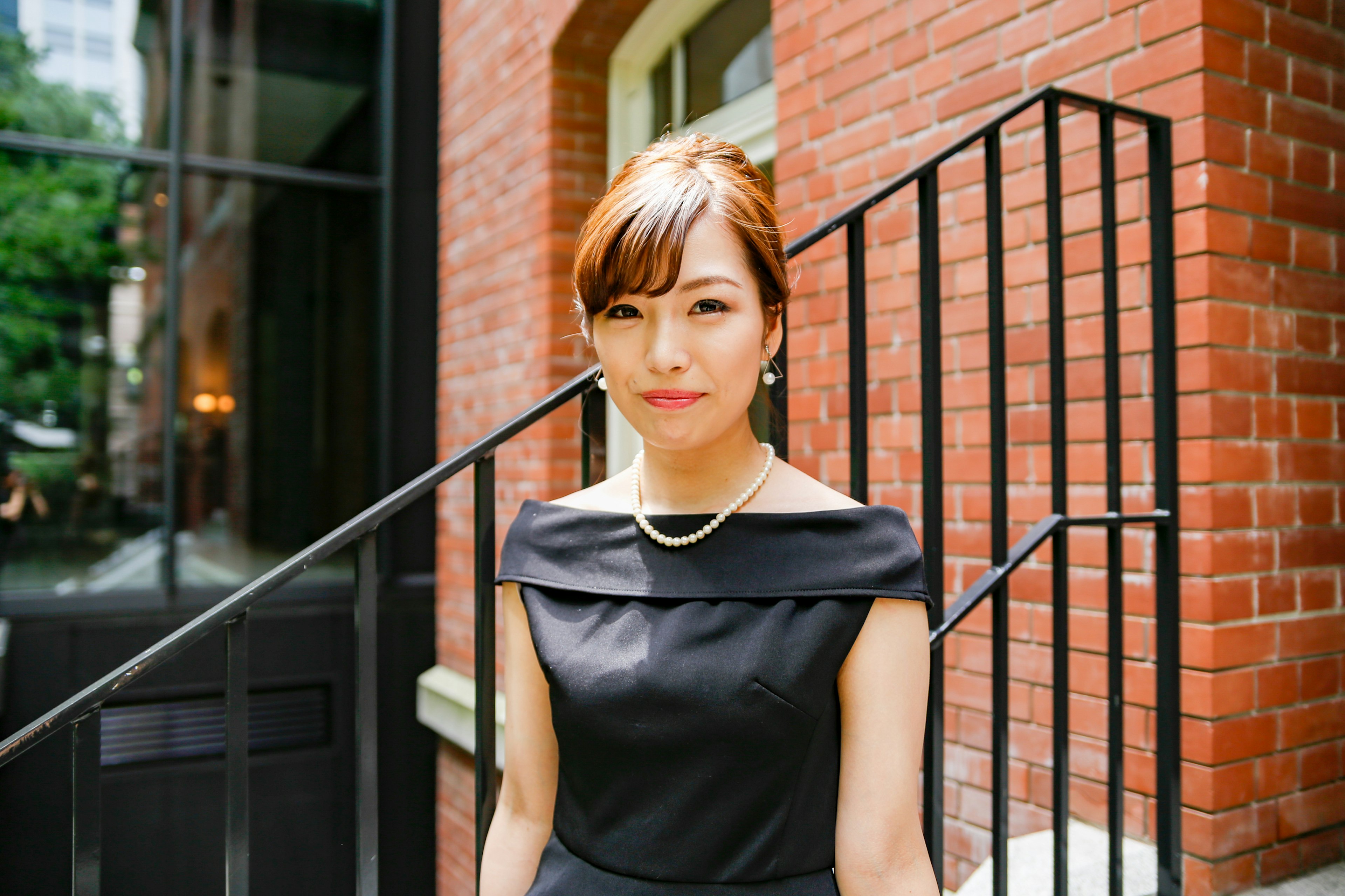 A woman in a black dress stands in front of a red brick building