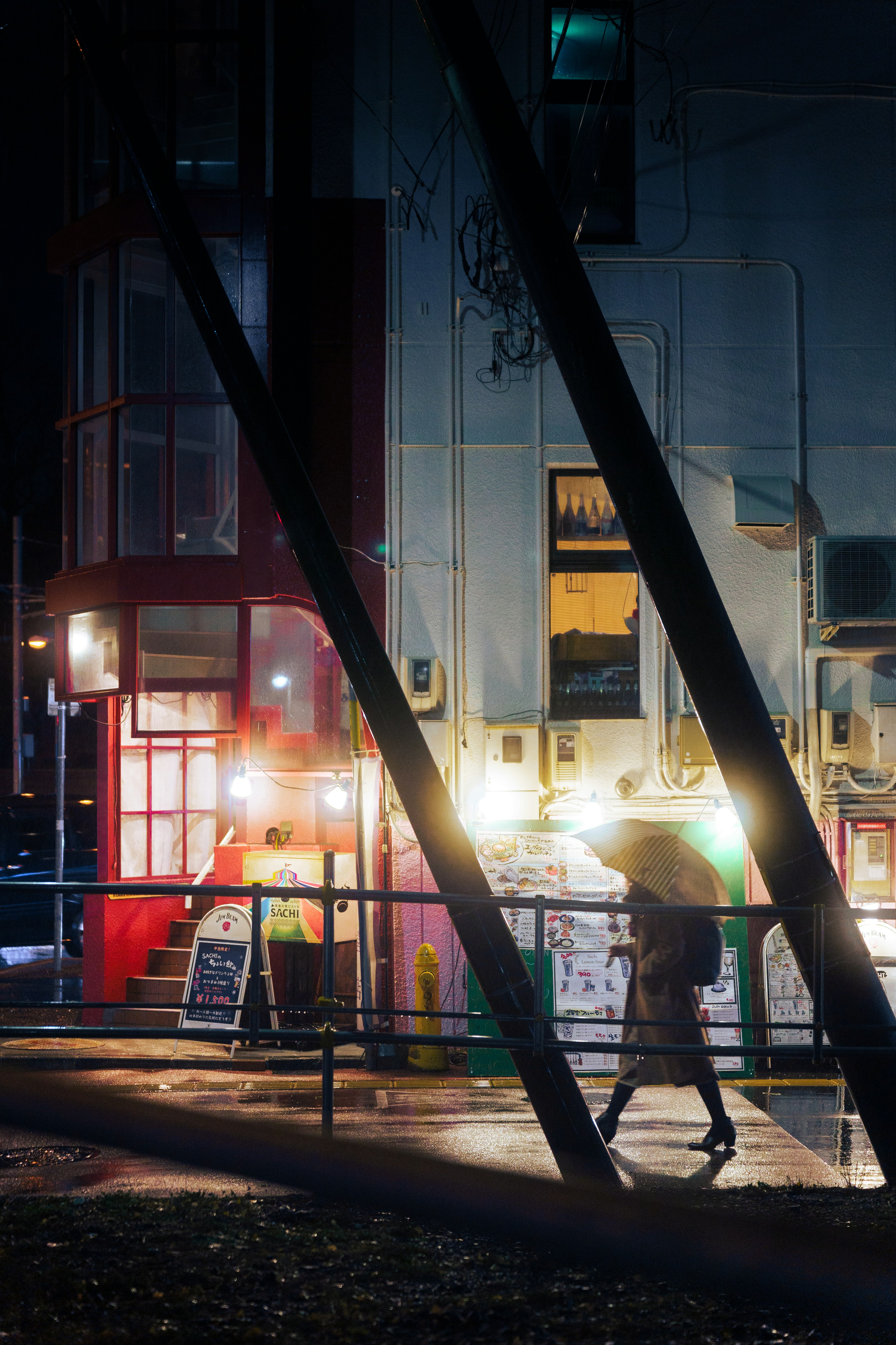 Escena urbana nocturna con un café iluminado y una persona con paraguas bajo la lluvia