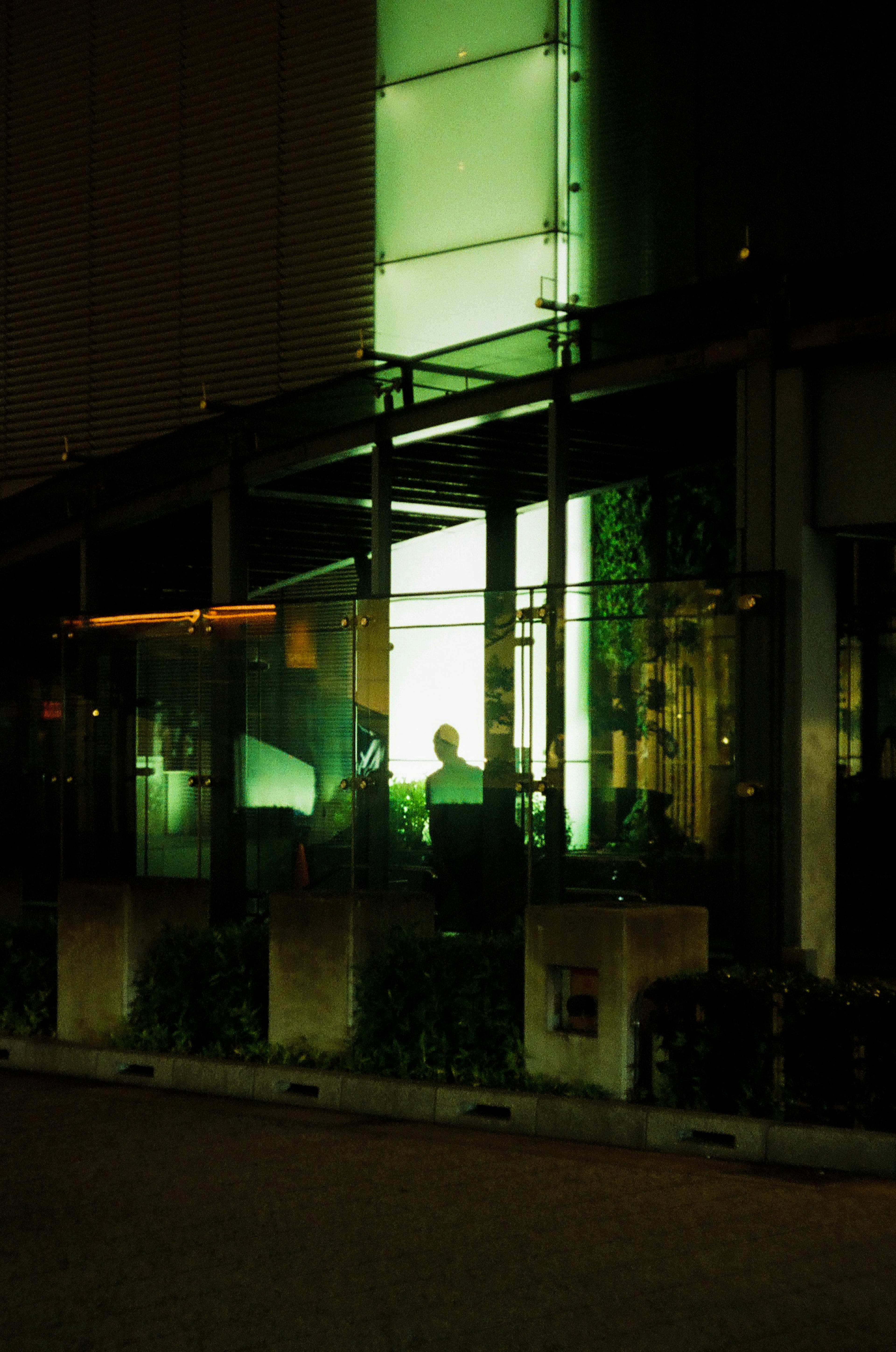 Silhouette d'une personne visible dans un bâtiment en verre éclairé par une lumière verte la nuit