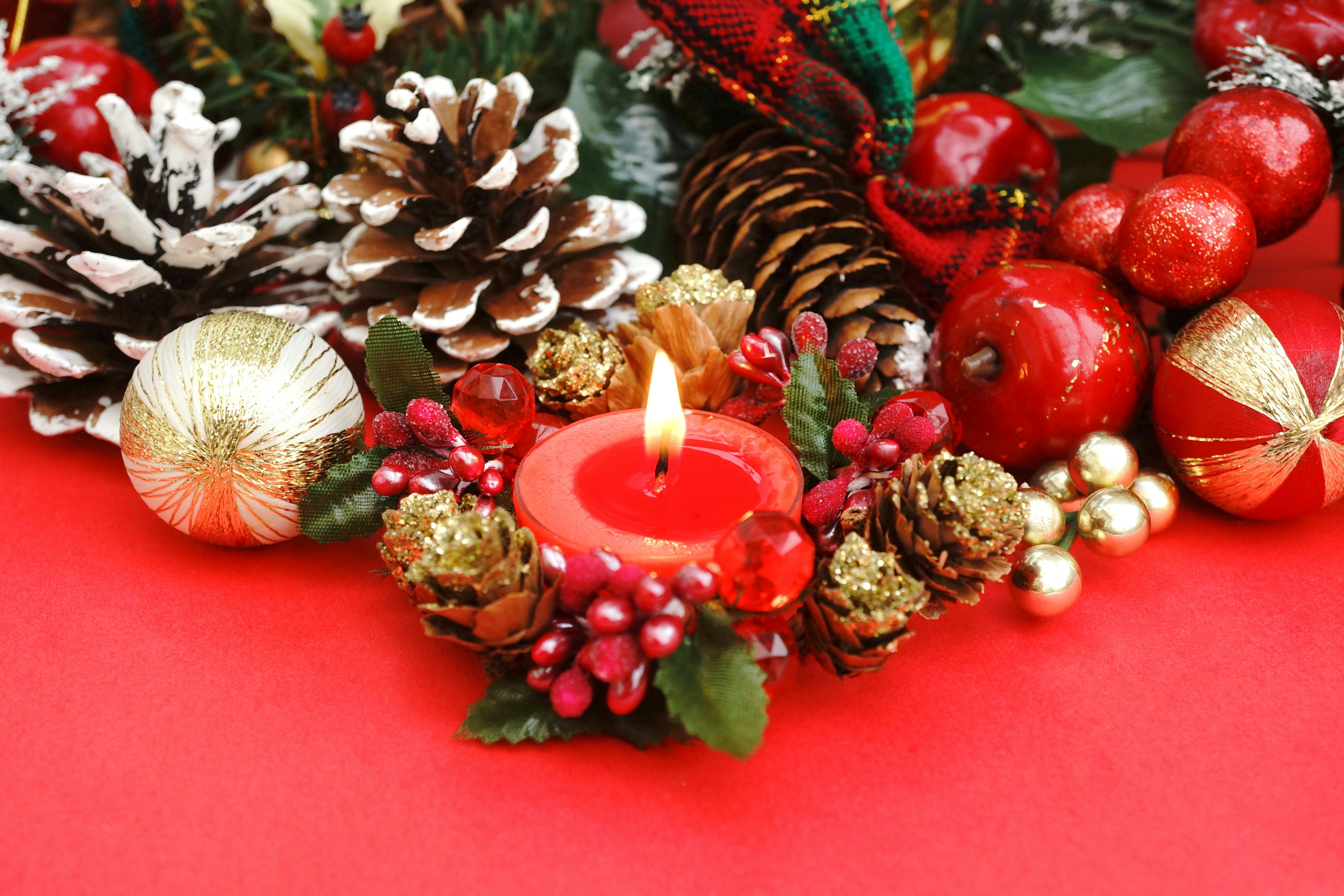 Christmas decoration featuring a candle and pine cones on a red background