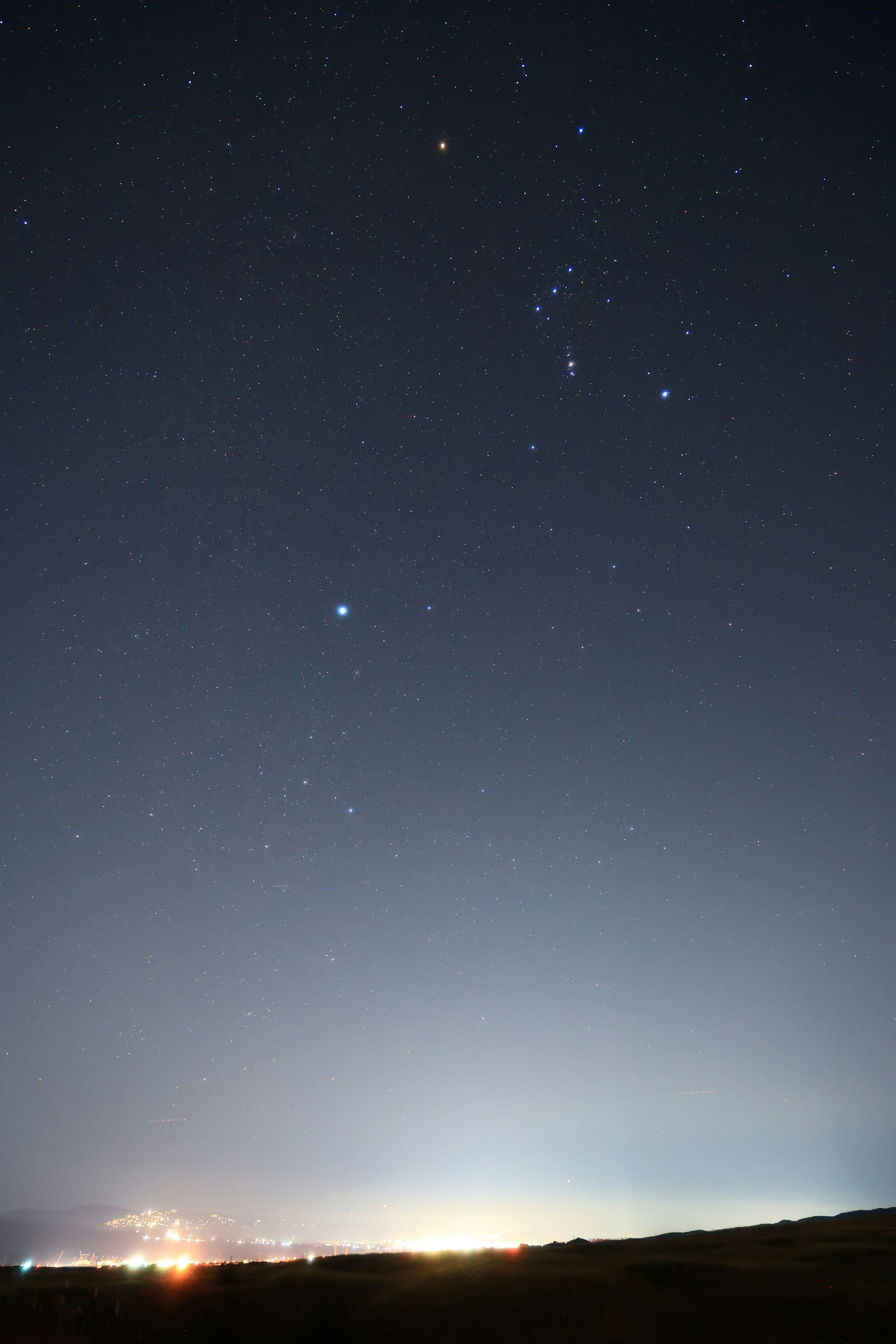 Cielo notturno pieno di stelle e luci della città in lontananza