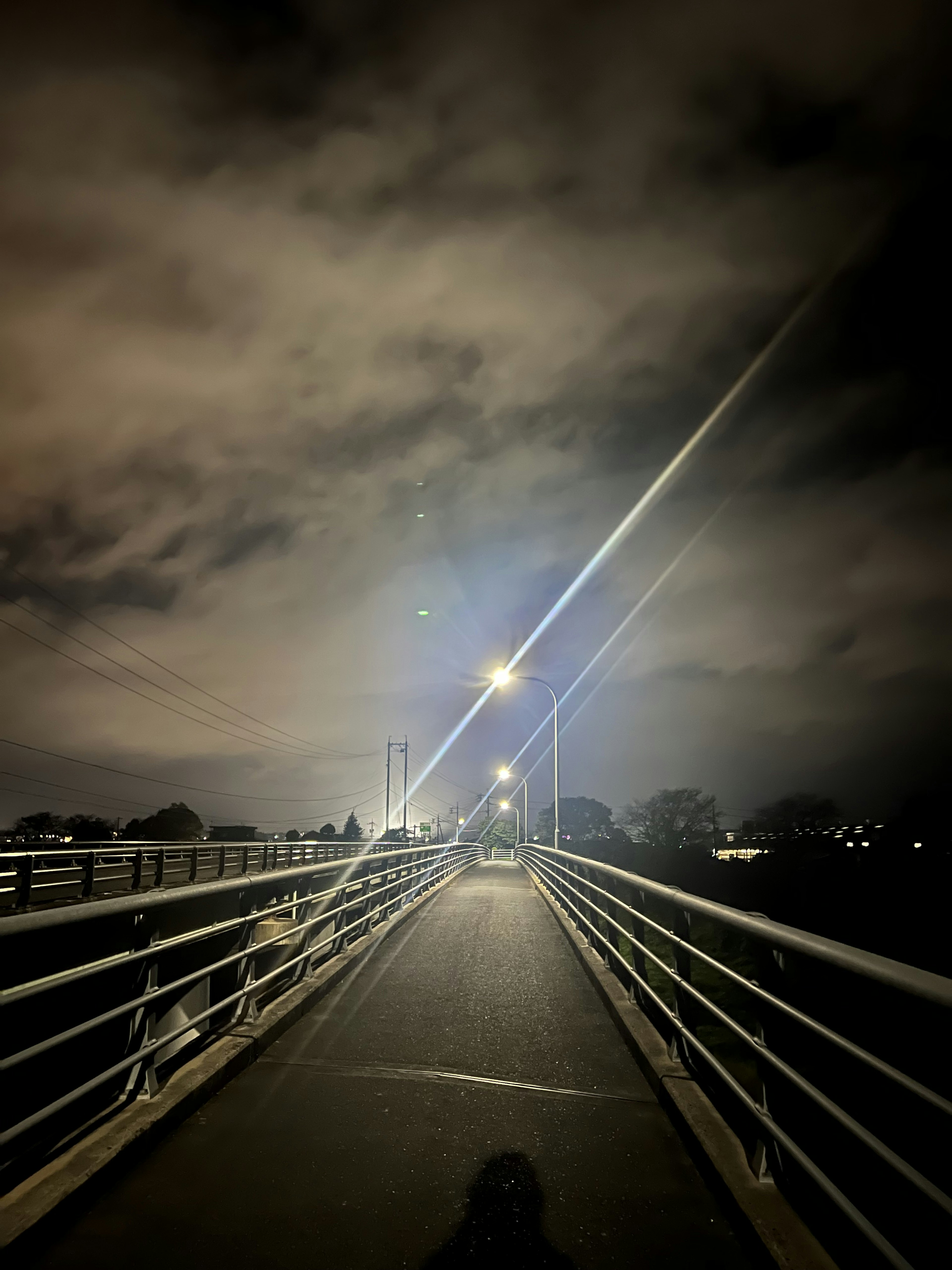 Pemandangan dari jembatan di malam hari dengan awan di langit dan lampu menerangi jalan menciptakan suasana tenang