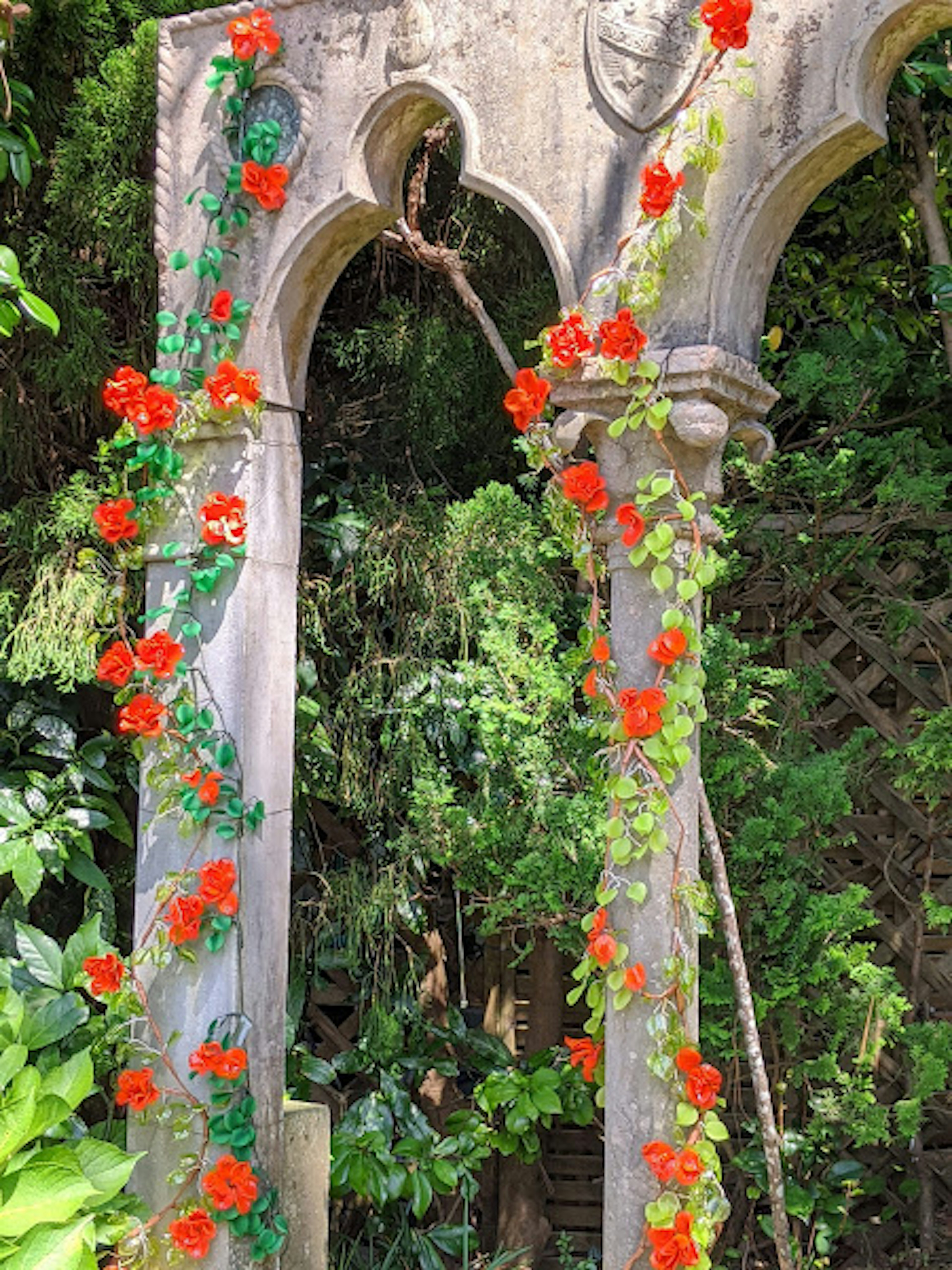 Old stone arch adorned with red flowers and surrounded by green foliage