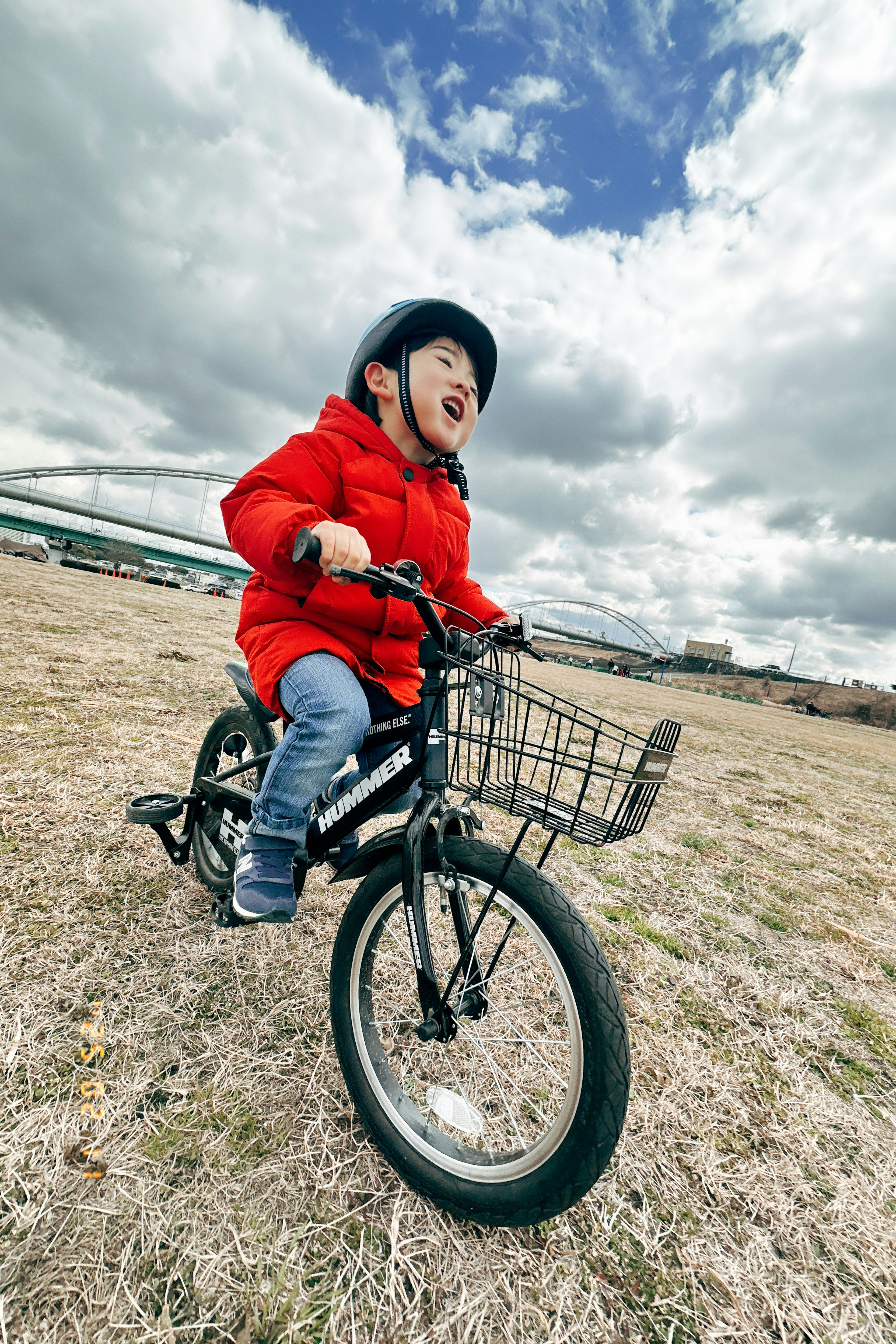 Bambino in cappotto rosso che va in bicicletta in una giornata di sole