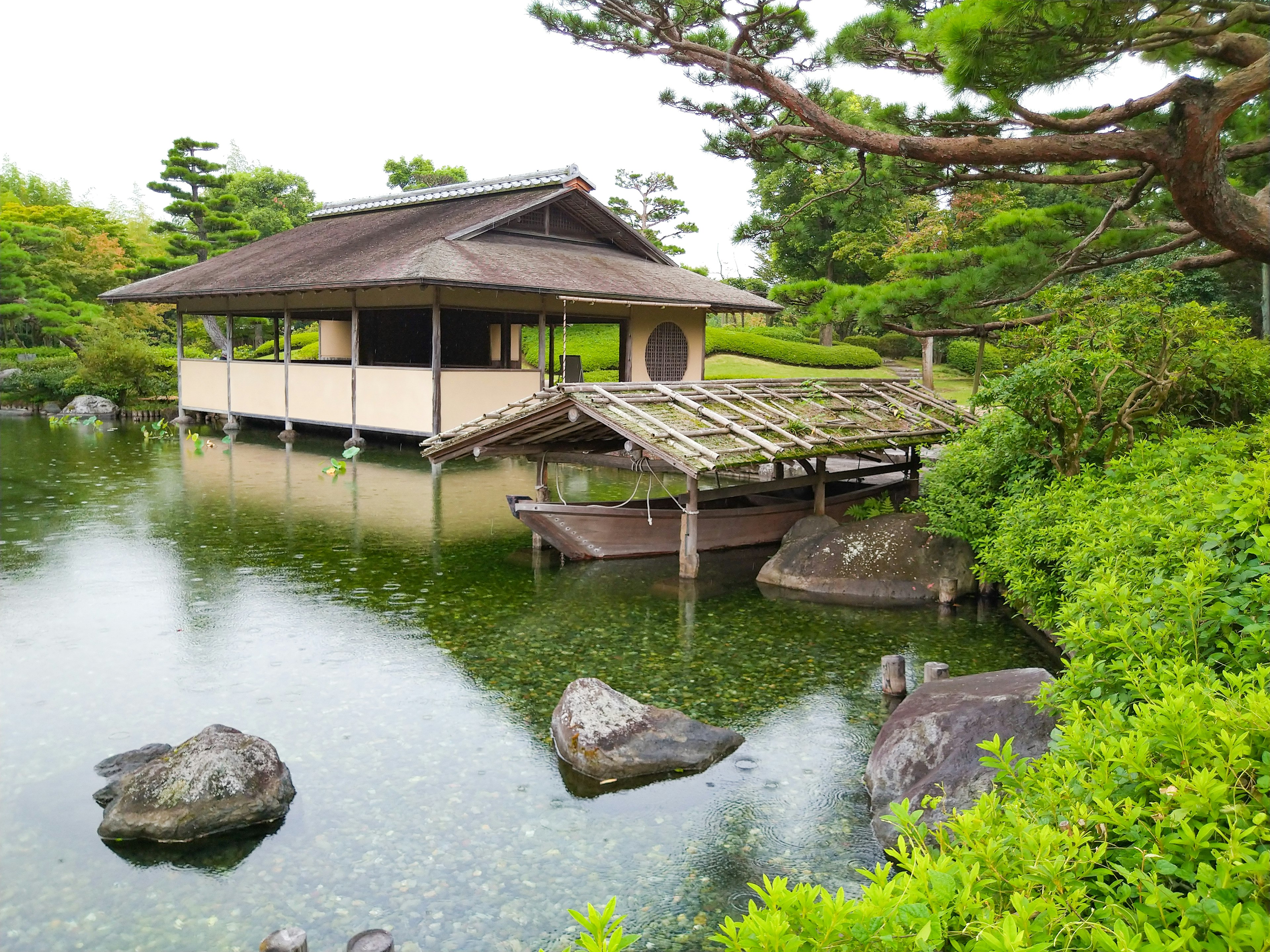 Rumah tradisional Jepang di samping kolam yang tenang dengan jembatan kayu