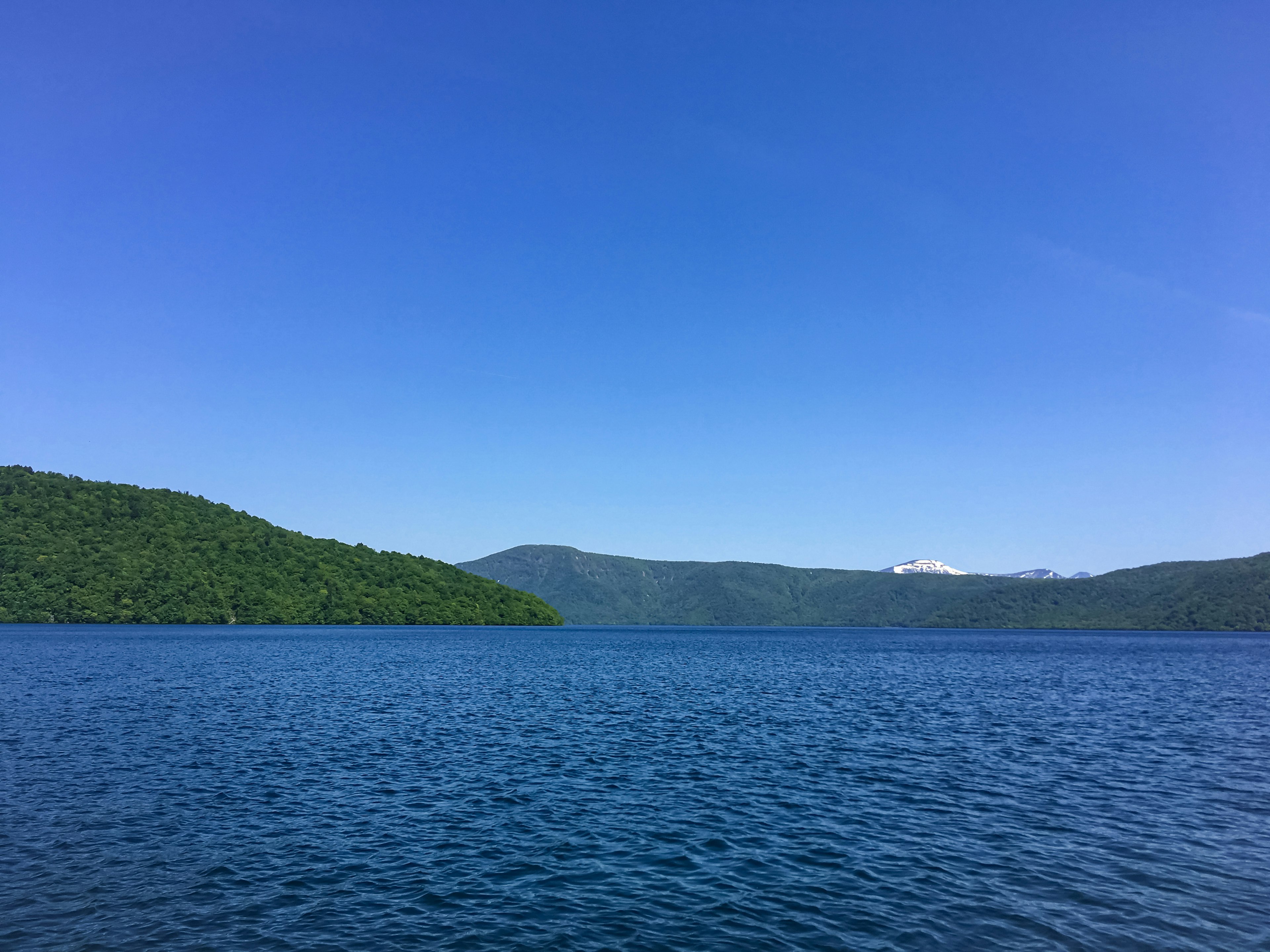 Scenic view of a calm lake surrounded by green mountains under a clear blue sky
