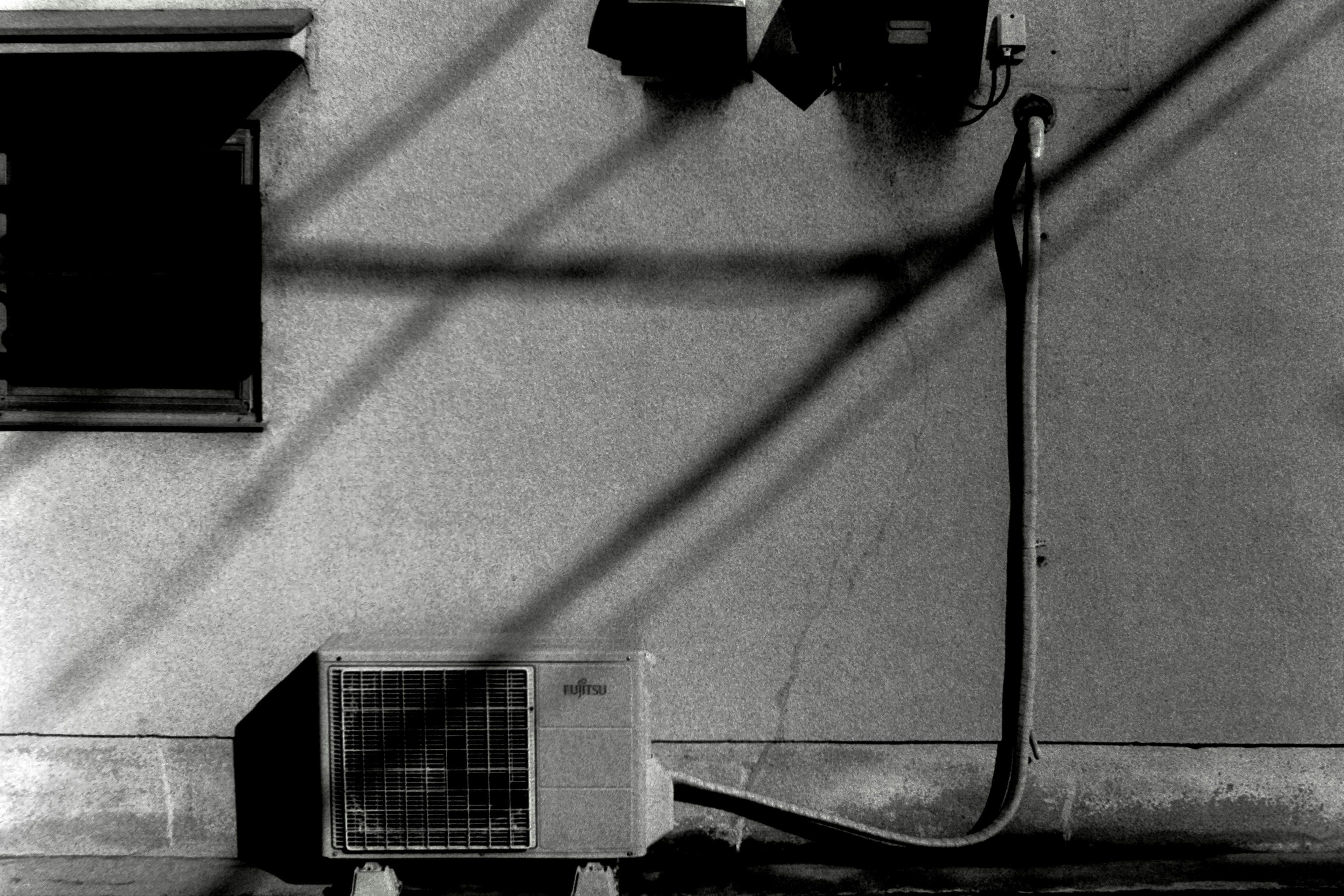 Black and white image of an air conditioning unit mounted on a wall with shadow patterns