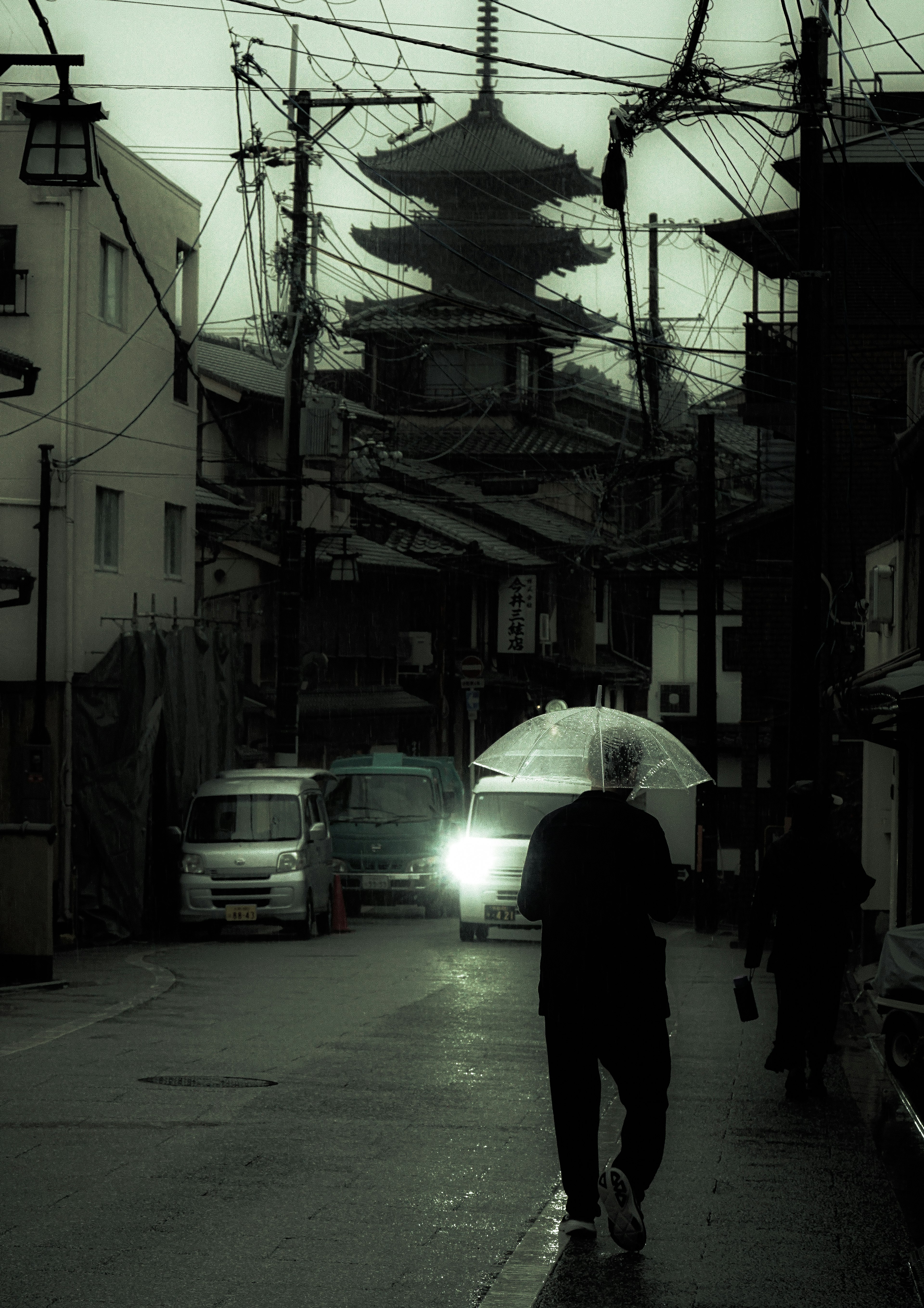 A person walking with an umbrella on a dimly lit street with a pagoda in the background