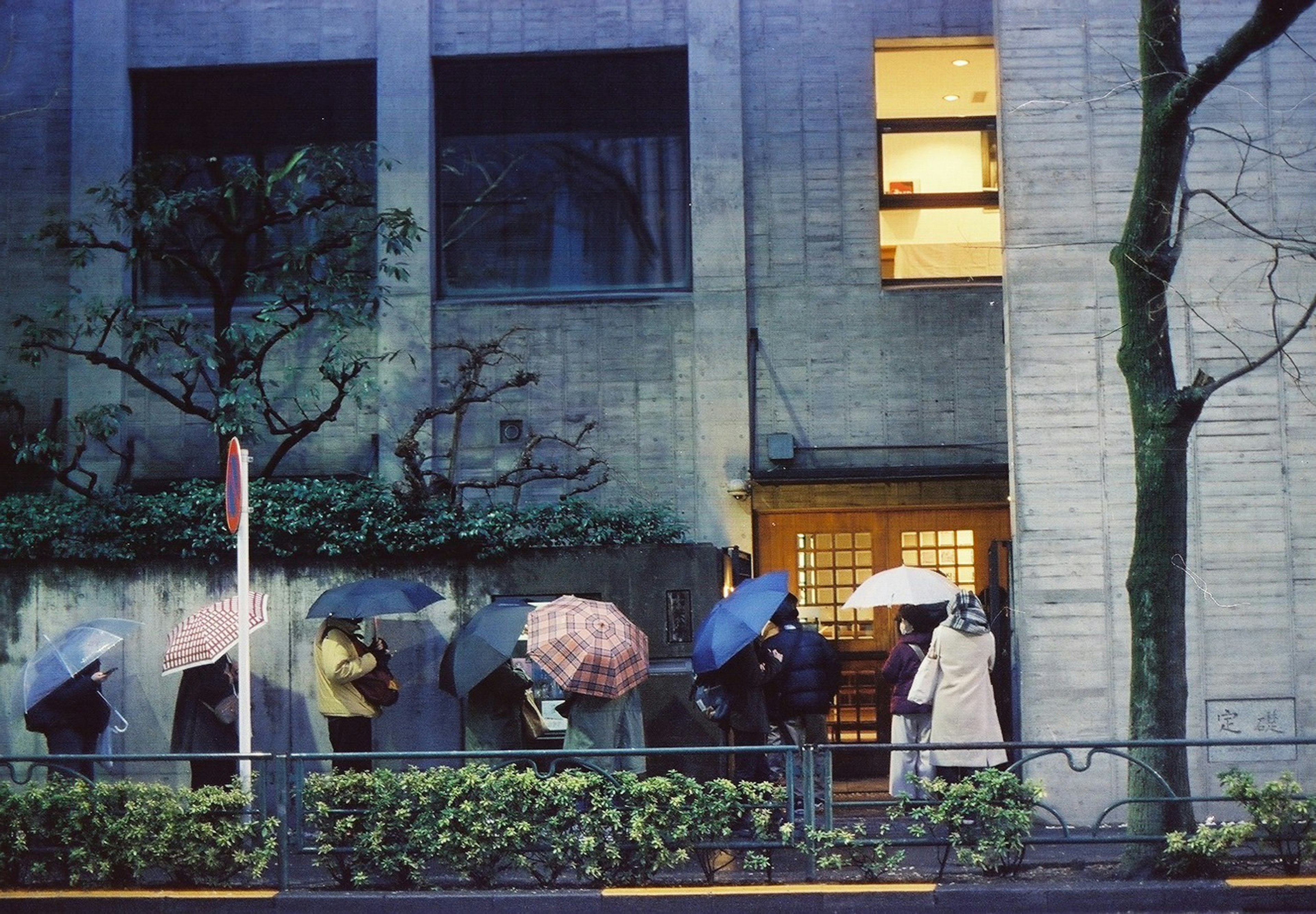 雨の中で傘を持つ人々が並ぶシーン 建物の前に立つ