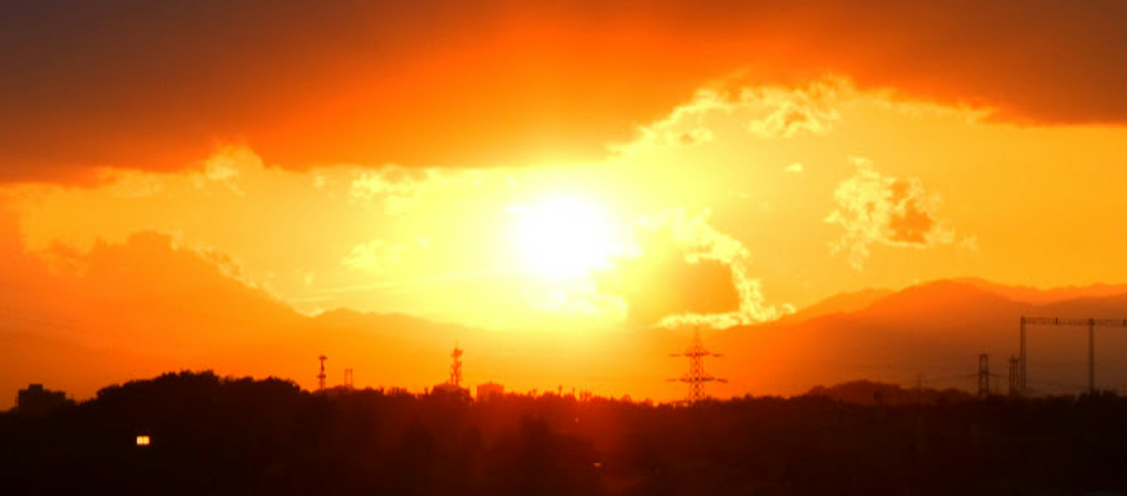 夕阳透过云彩闪耀，山脉和电线以剪影形式出现