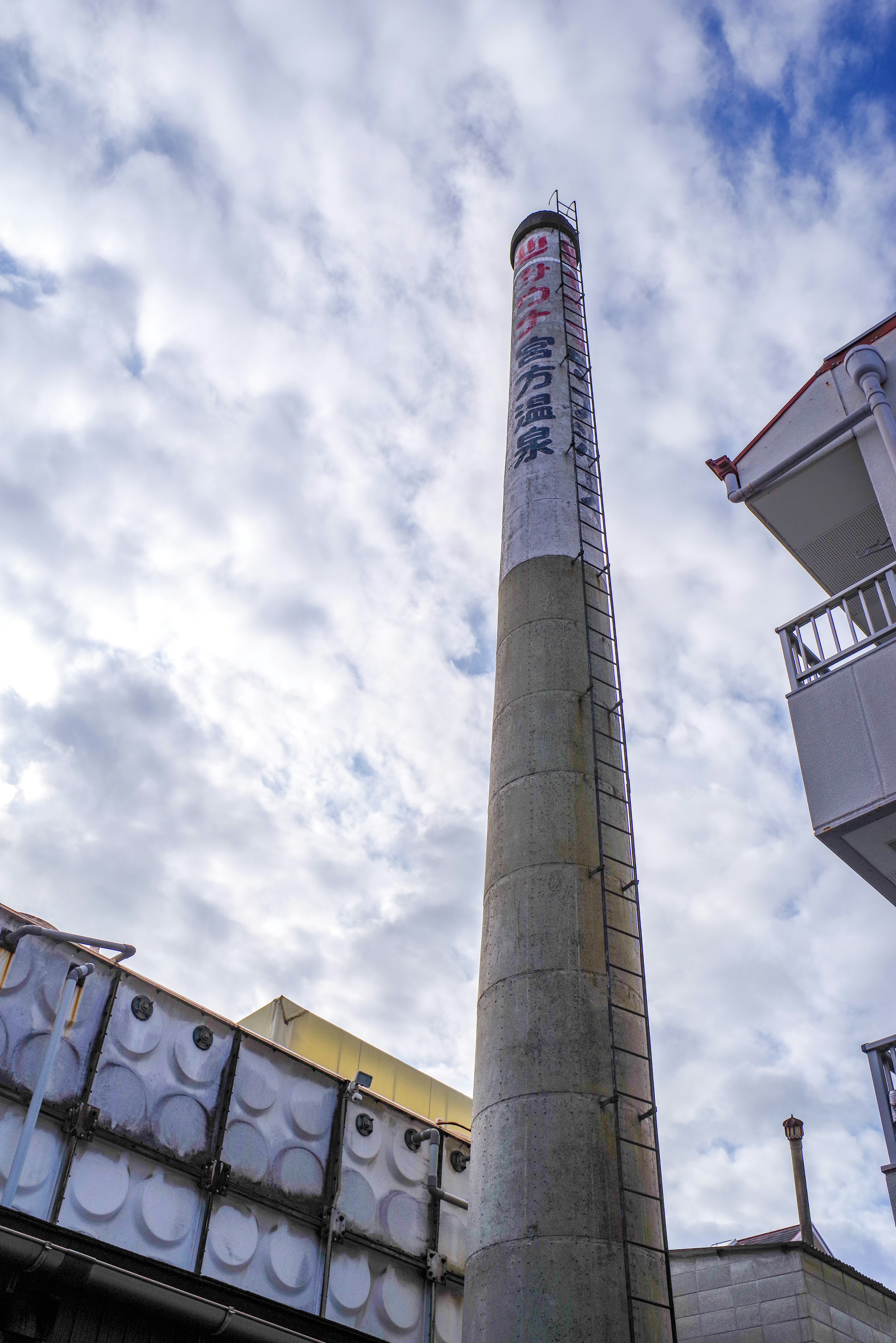 Industrielandschaft mit hohem Schornstein vor blauem Himmel und Wolken