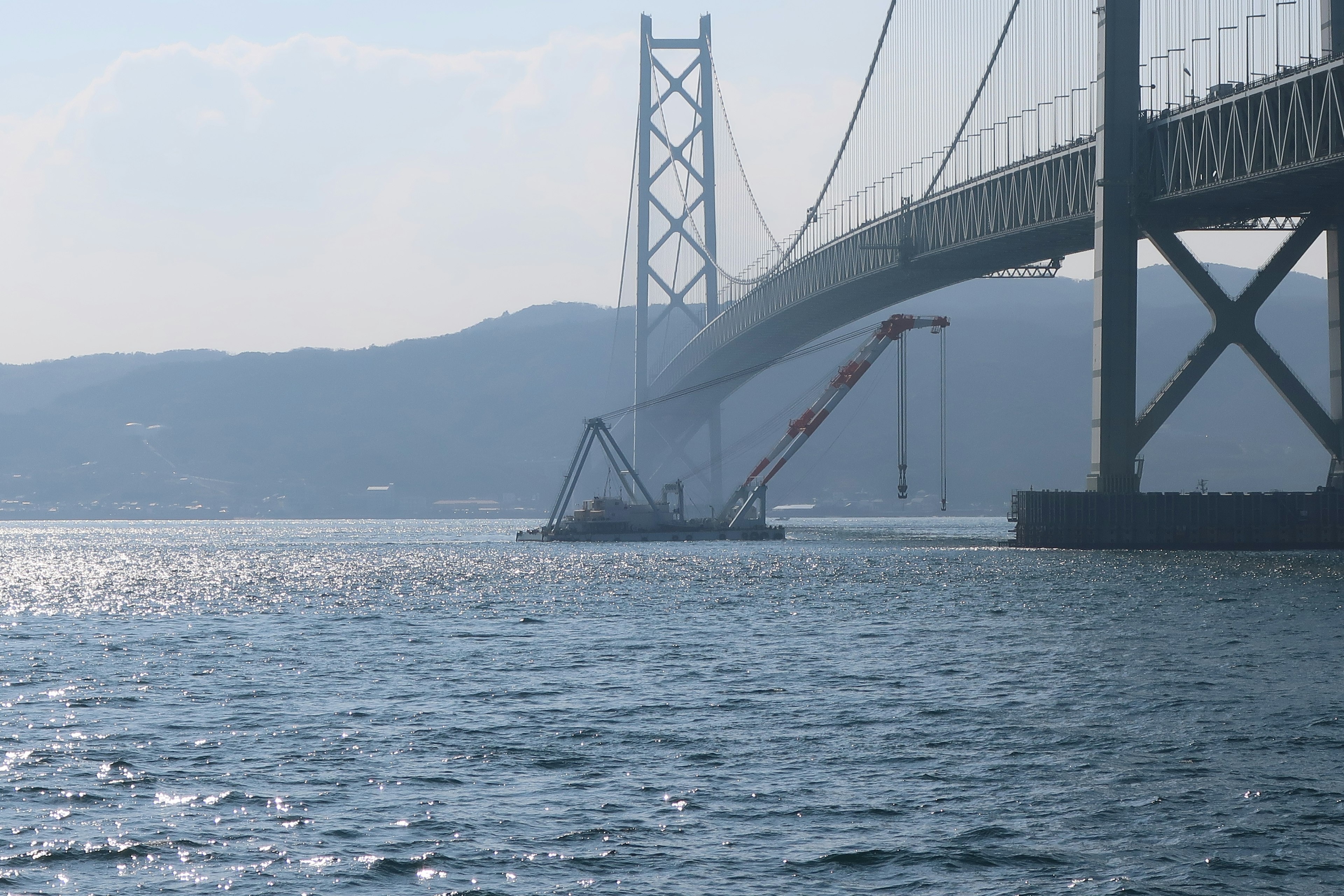 View of a crane vessel working under a bridge over the sea