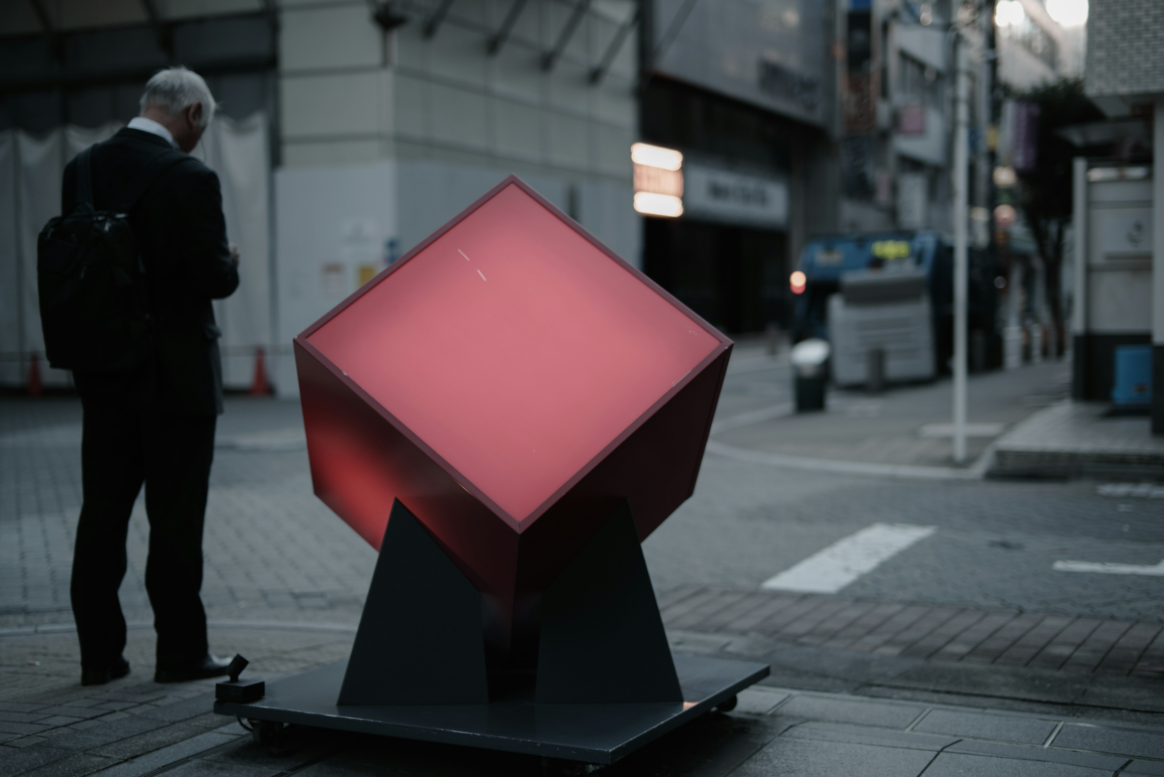 Una scultura cubica rossa con un uomo in giacca che sta in strada